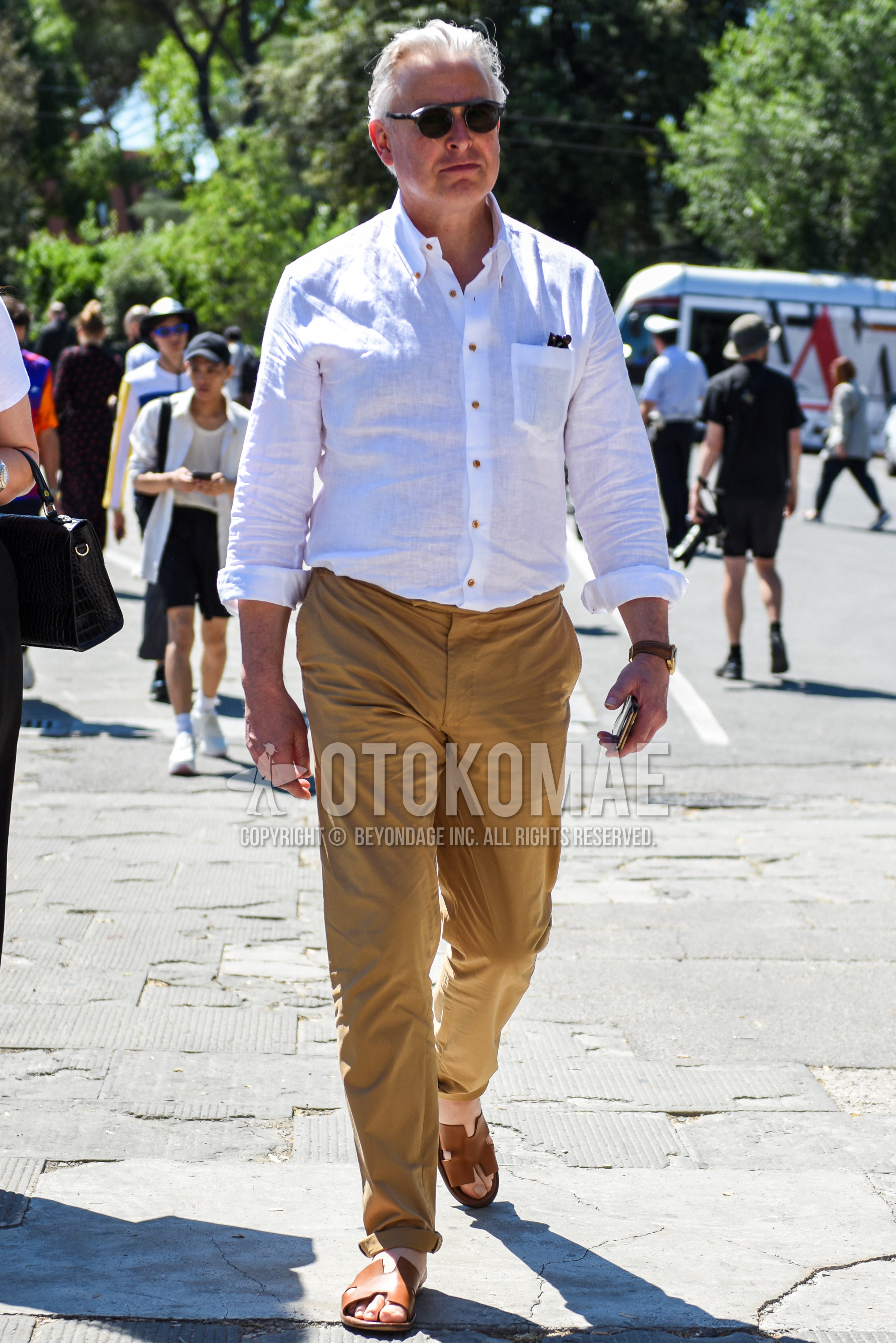 Men's spring summer outfit with gray plain sunglasses, white plain shirt, beige plain chinos, brown leather sandals.