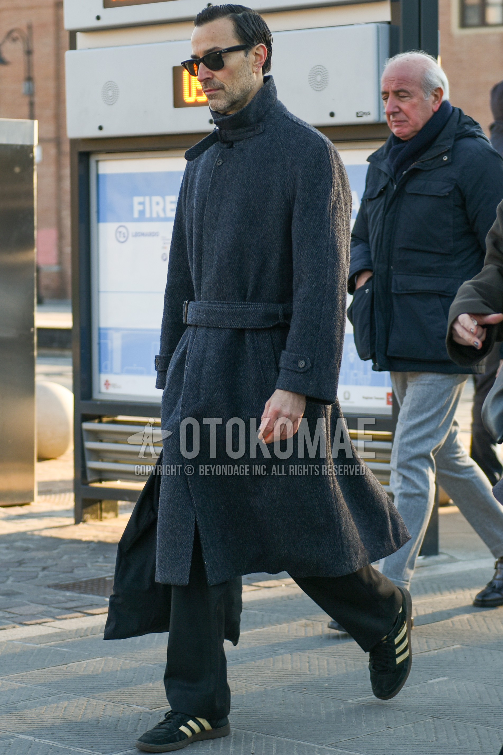 Men's autumn winter outfit with black plain sunglasses, gray plain belted coat, gray plain slacks, black low-cut sneakers.