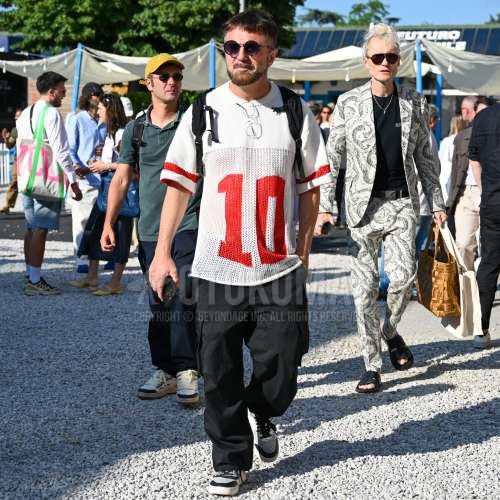 黒無地のサングラス、シルバー無地のメガネ、メッシュ　ニットの白レタードのTシャツ、黒無地のカーゴパンツ、白ローカットのスニーカー、黒無地のバックパックを合わせた夏春のメンズコーデ・着こなし。