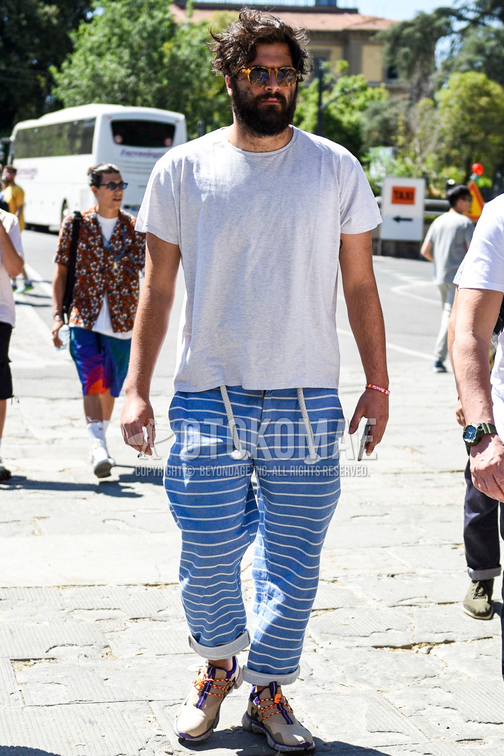 Men's summer outfit with beige tortoiseshell sunglasses, white plain t-shirt, blue horizontal stripes easy pants, beige low-cut sneakers.