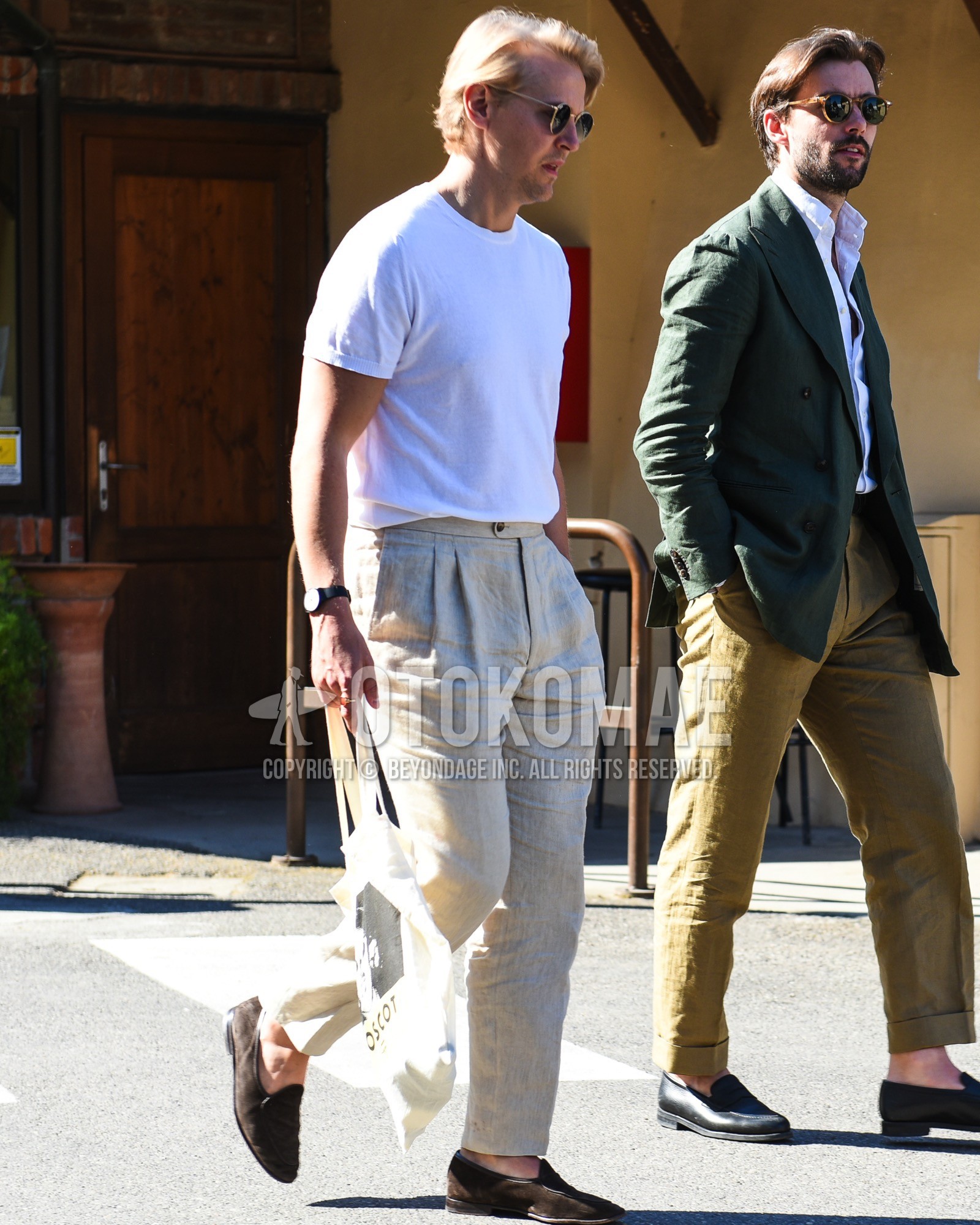 Men's spring summer outfit with gold plain sunglasses, white plain t-shirt, beige plain slacks, brown  loafers leather shoes, white graphic tote bag.