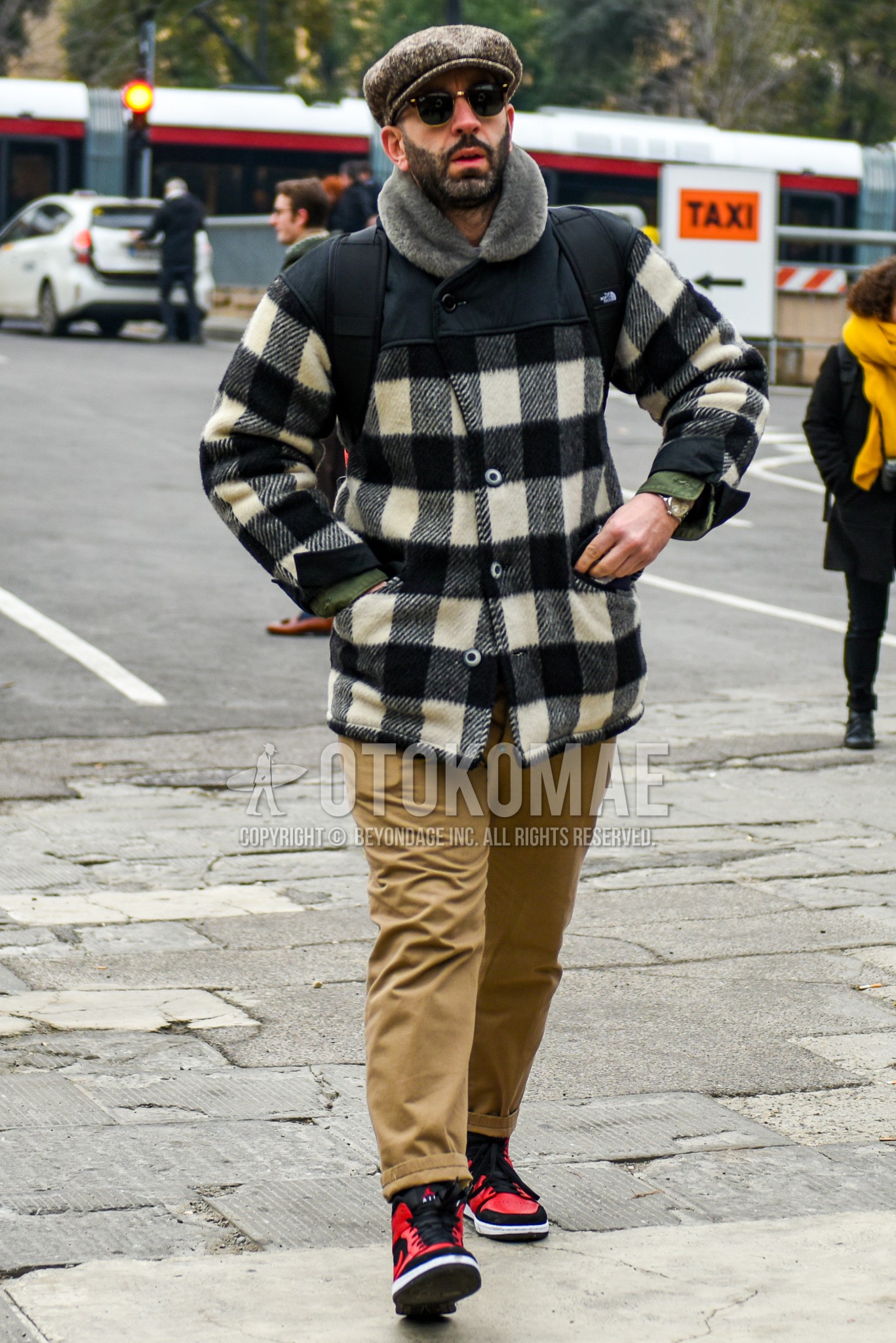 Men's autumn winter outfit with beige cap, black plain sunglasses, white black check outerwear, beige plain chinos, red black high-cut sneakers.