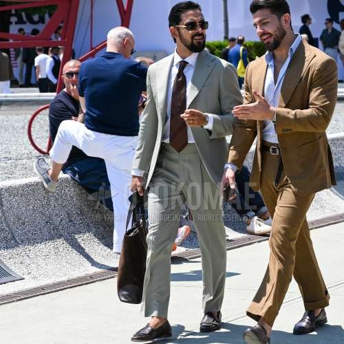 ゴールド無地のサングラス、白無地のシャツ、グレー無地のベルトレスパンツ、ブラウンモンクシューズの革靴、レザーのブラウン無地のブリーフケース/ハンドバッグ、グレー無地のスーツ、レッド・グリーンレジメンタルのネクタイを合わせた夏春のメンズコーデ・着こなし。