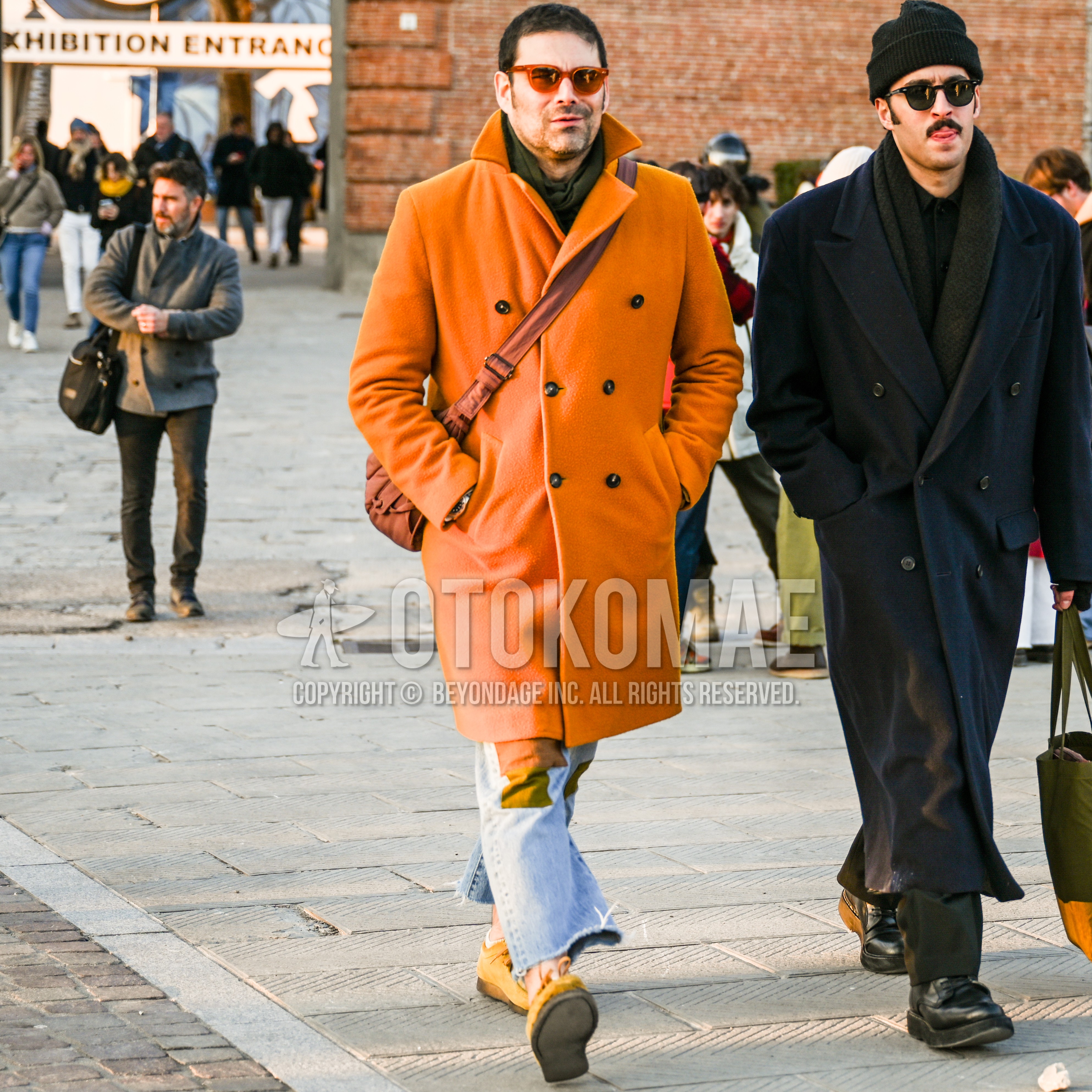 Men's autumn winter outfit with clear orange plain sunglasses, olive green plain scarf, orange plain chester coat, plain denim/jeans, brown suede shoes leather shoes, orange plain shoulder bag.