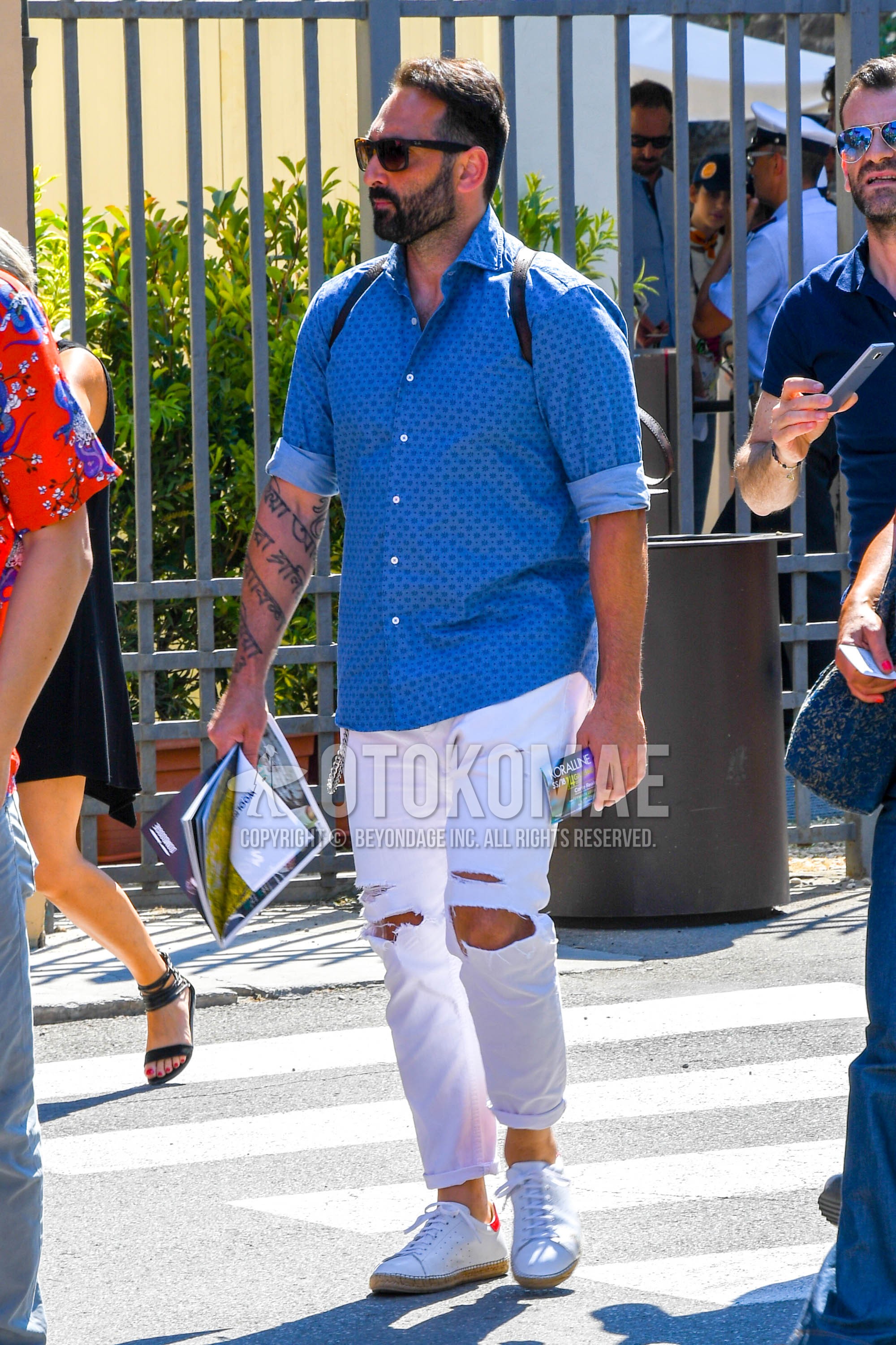 Men's spring summer autumn outfit with plain sunglasses, blue light blue plain shirt, white plain damaged jeans, white low-cut sneakers.
