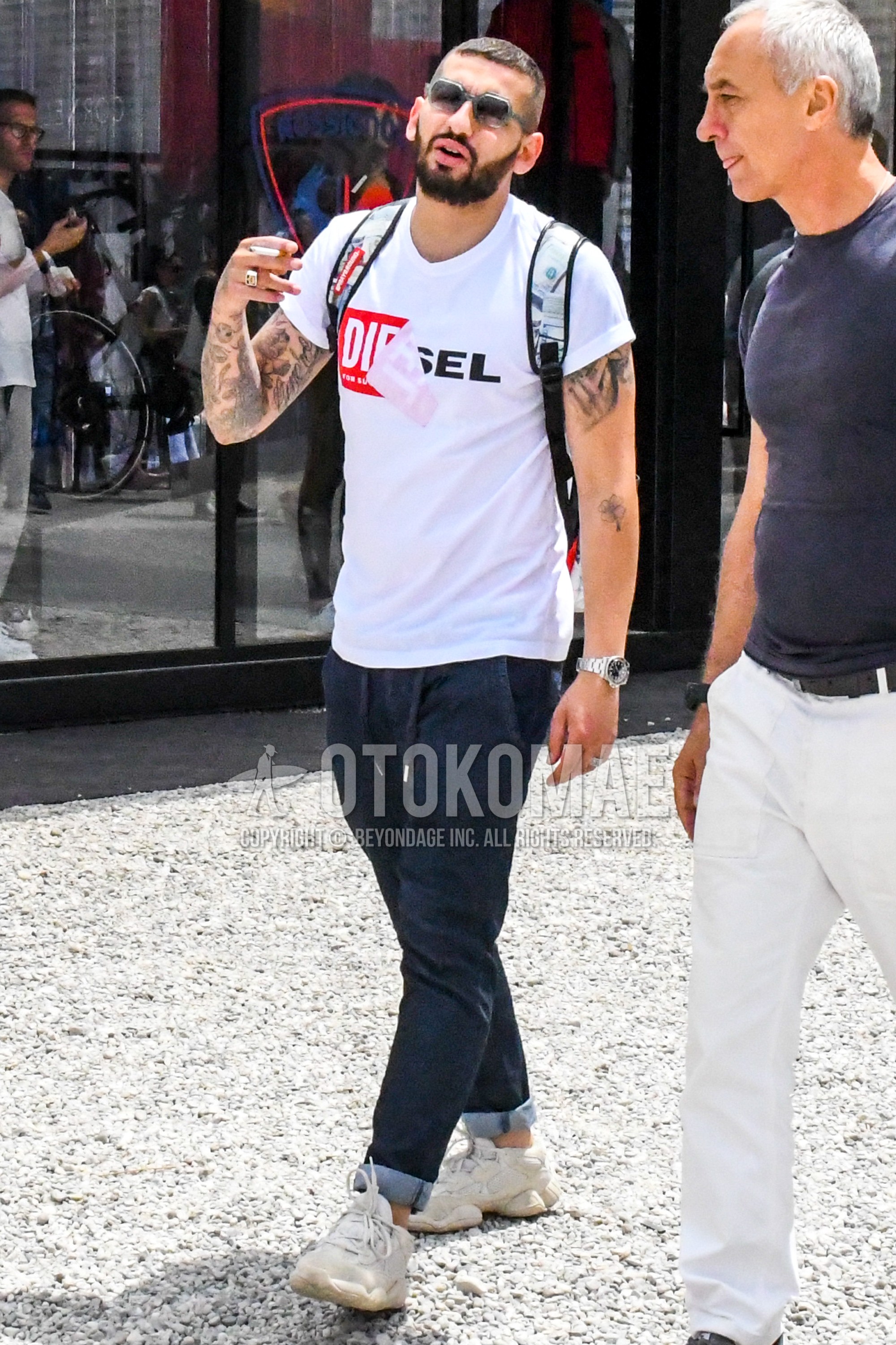 Men's summer outfit with clear plain sunglasses, white graphic t-shirt, dark gray plain easy pants, white low-cut sneakers.