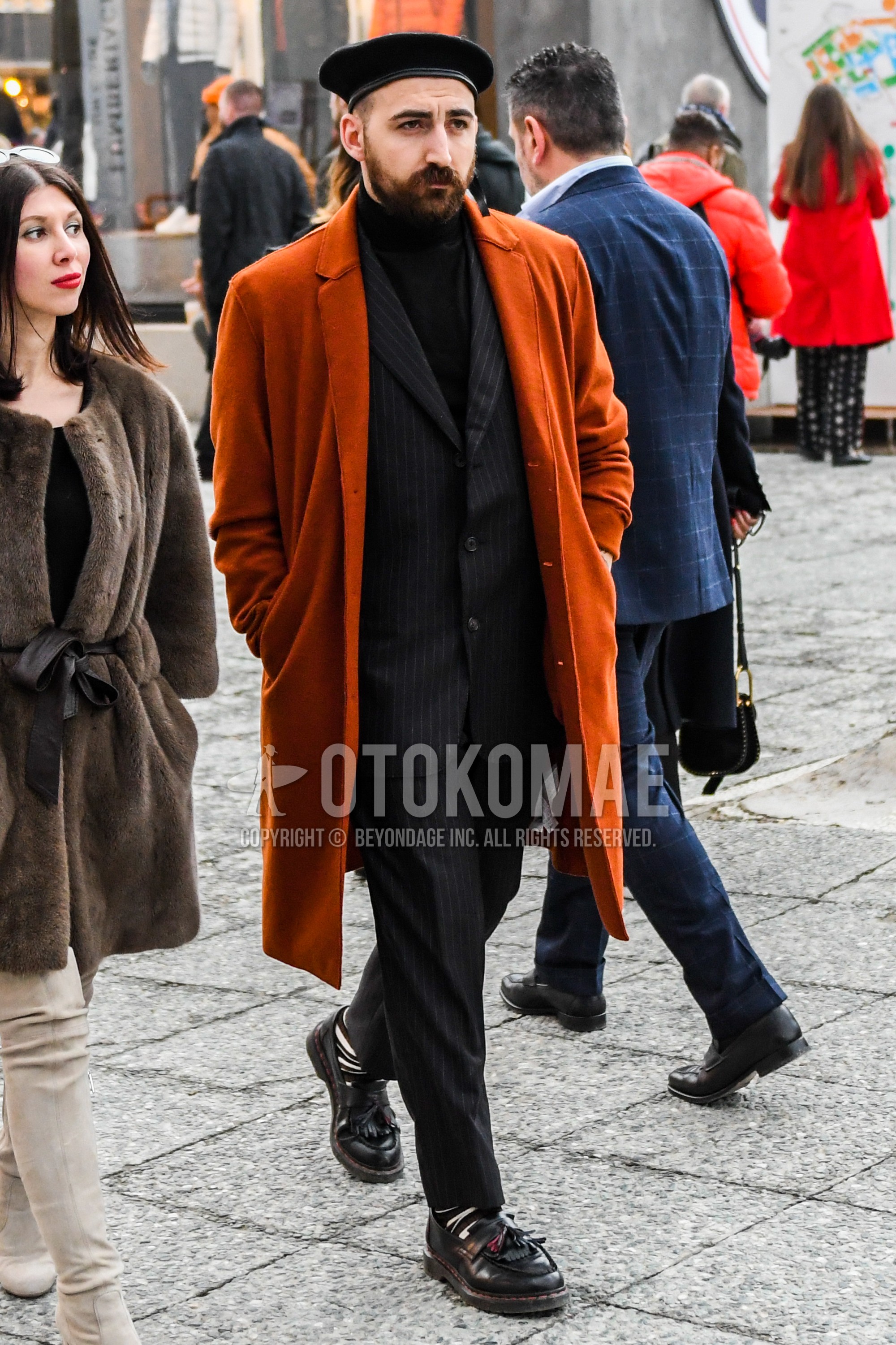 Men's winter outfit with orange plain chester coat, black plain sweater, white brown horizontal stripes socks, brown tassel loafers leather shoes, black stripes suit.
