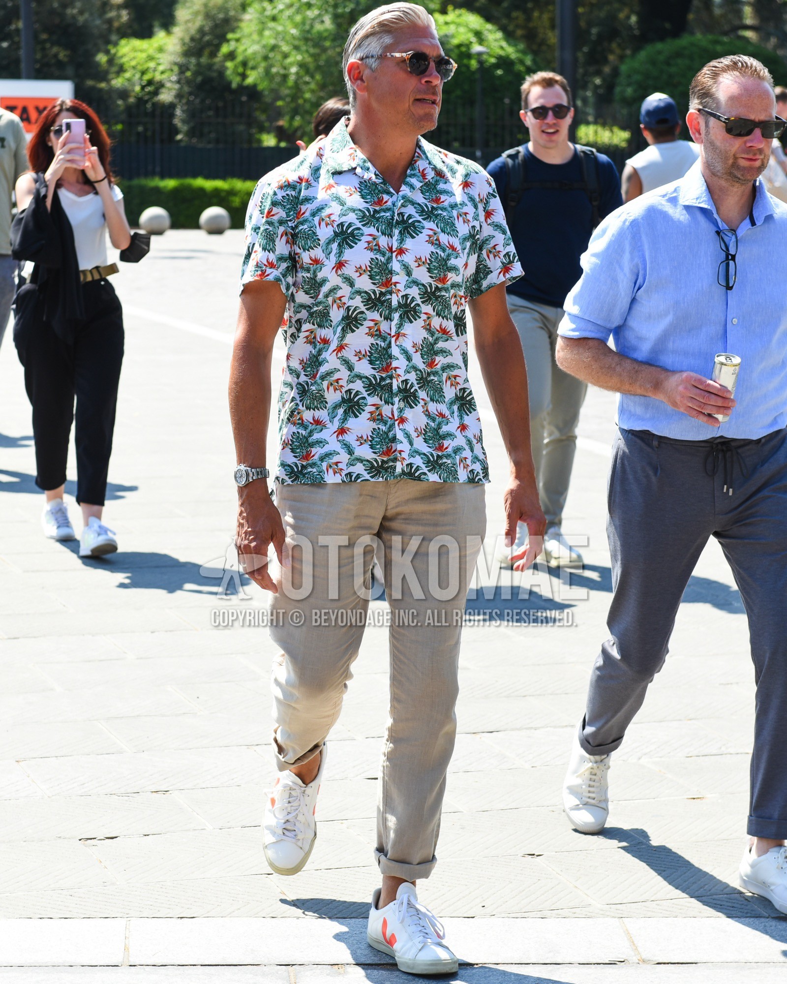 Men's spring summer outfit with brown tortoiseshell sunglasses, white graphic shirt, beige plain chinos, white low-cut sneakers.