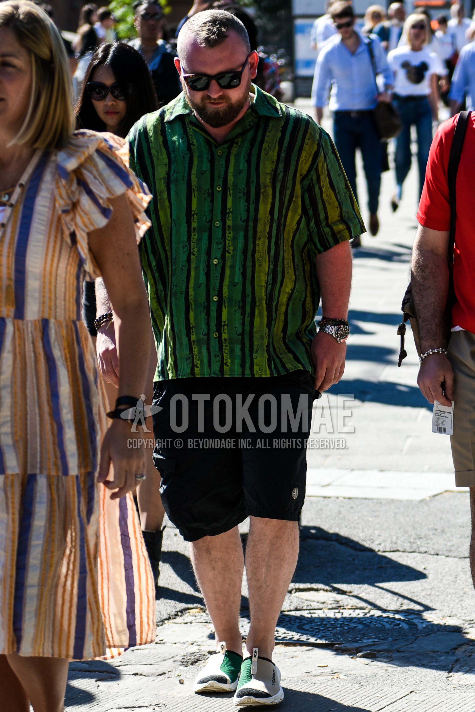 Men's summer outfit with black plain sunglasses, green stripes shirt, black plain short pants, green low-cut sneakers.