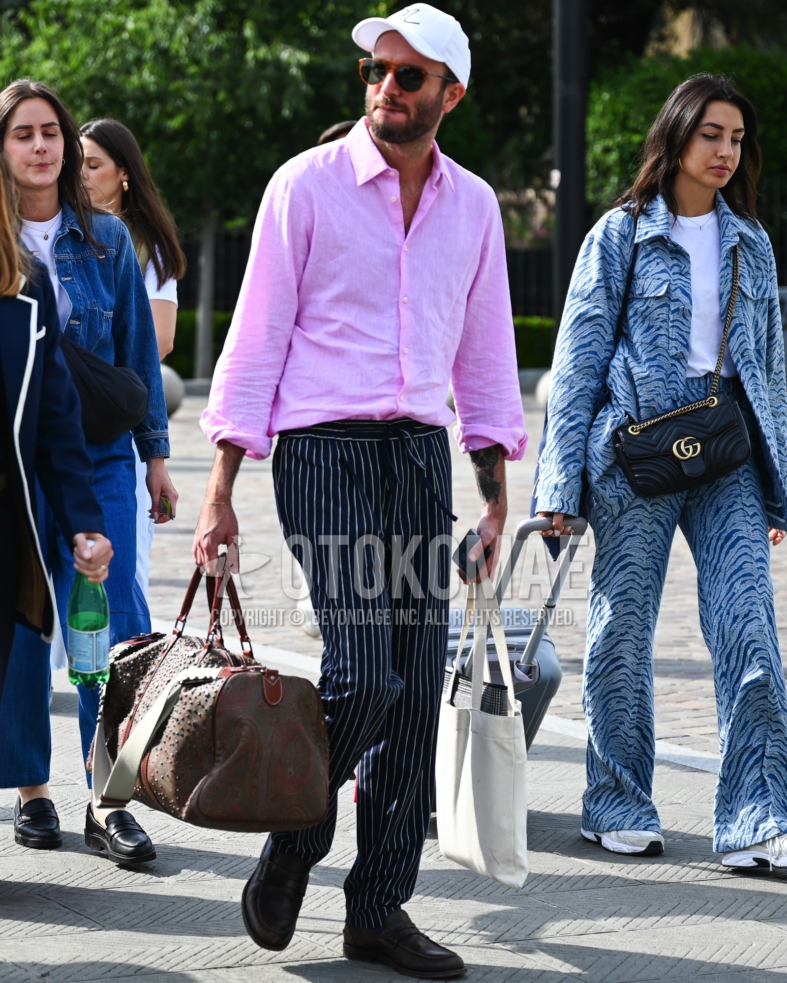 Men's spring summer autumn outfit with white one point baseball cap, black plain sunglasses, pink plain shirt, navy stripes slacks, brown coin loafers leather shoes, brown plain boston bag.