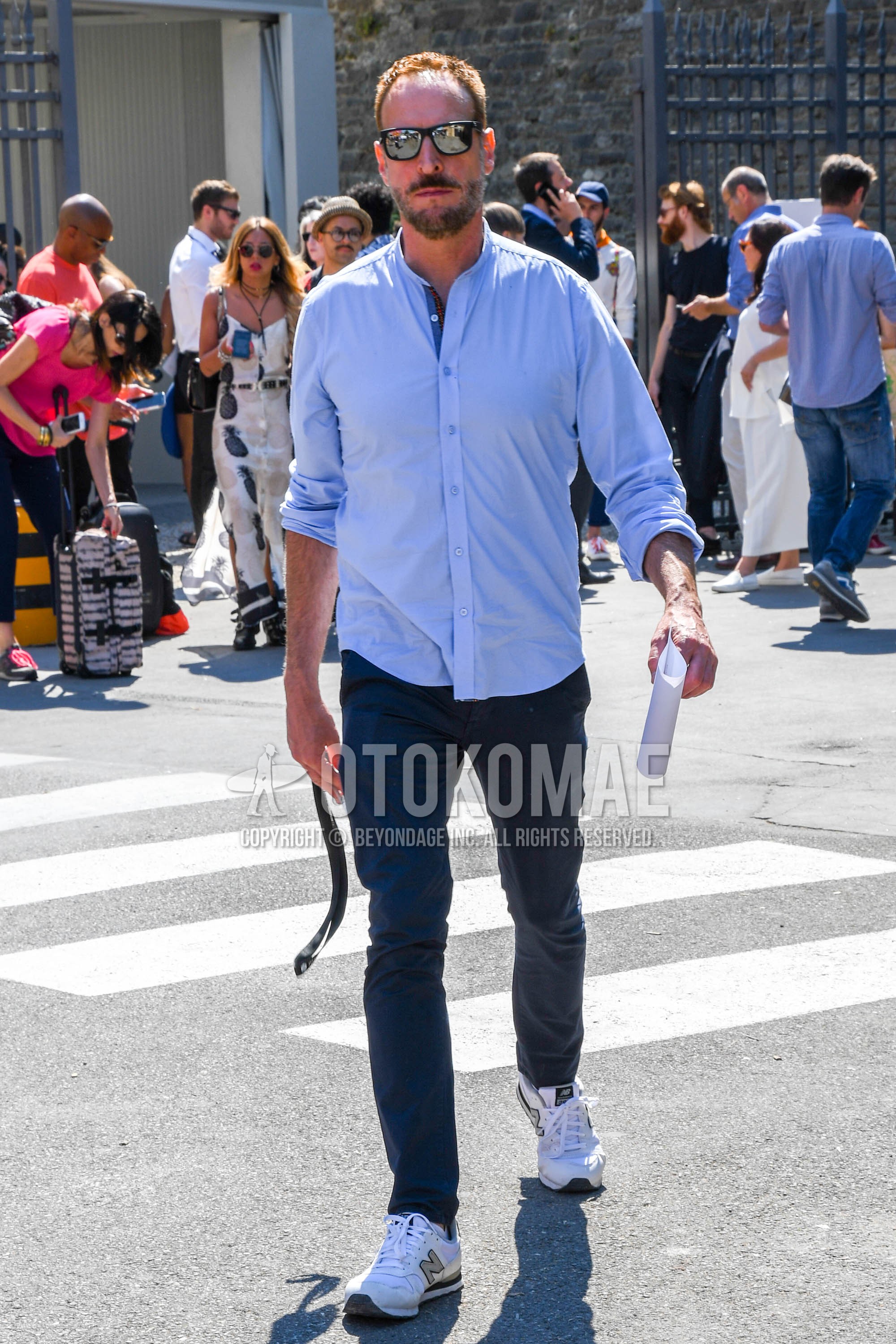 Men's spring summer outfit with plain sunglasses, light blue plain shirt, navy plain chinos, white low-cut sneakers.