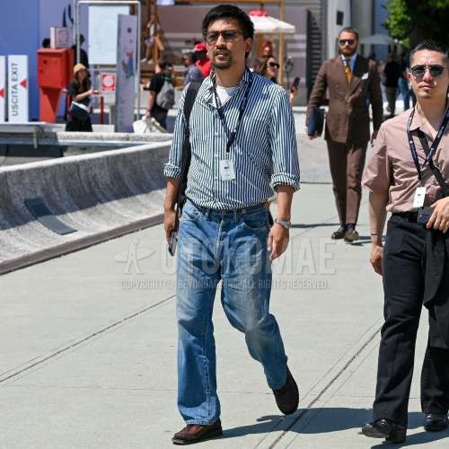 クリア・グレー無地のサングラス、黒・白ストライプのシャツ、白無地のTシャツ、ブルー無地のデニム/ジーンズ、ブラウンモカシン/デッキシューズの革靴、黒無地のバックパックを合わせた春夏のメンズコーデ・着こなし。