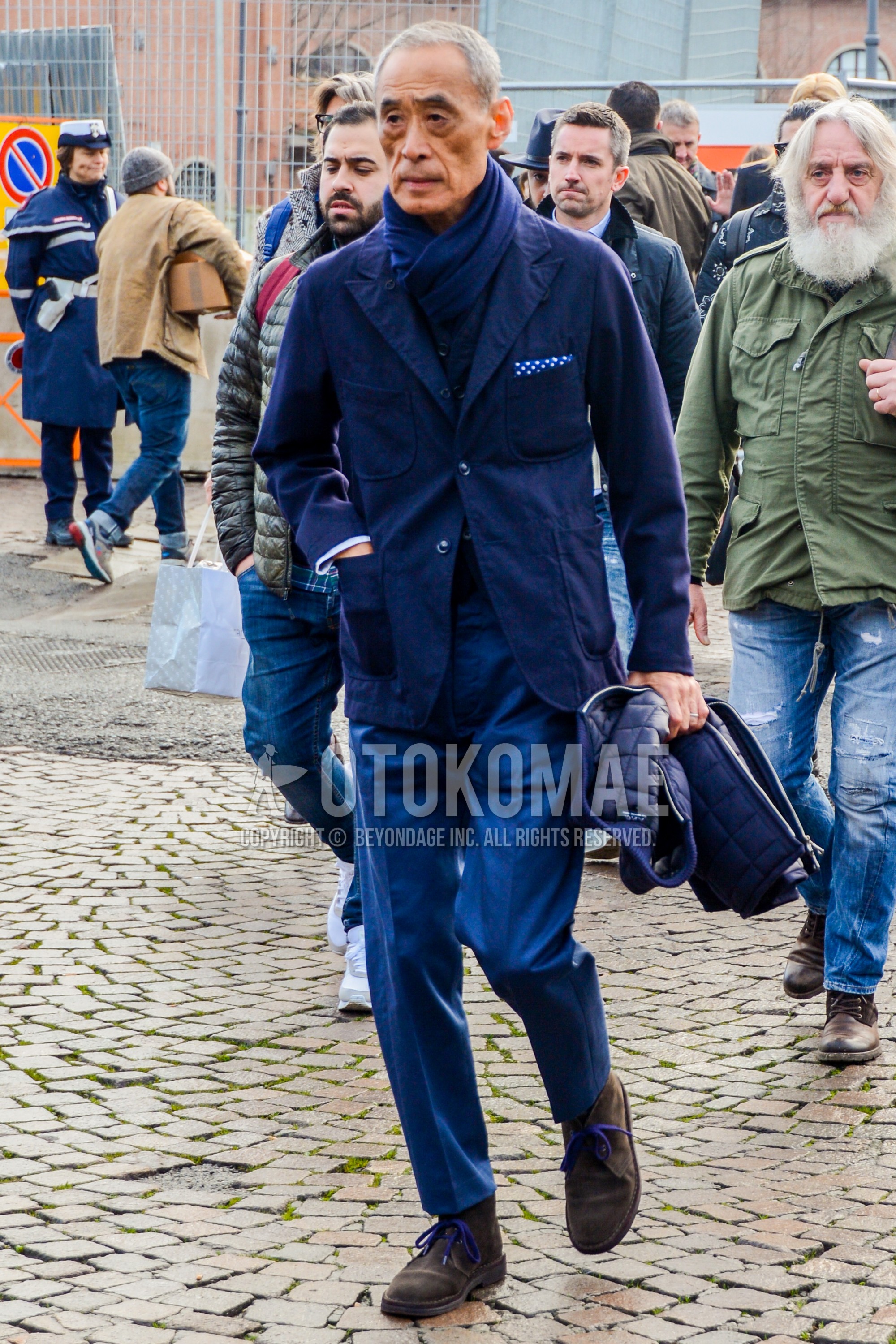 Men's winter outfit with plain scarf, navy plain tailored jacket, blue plain slacks, brown chukka boots.