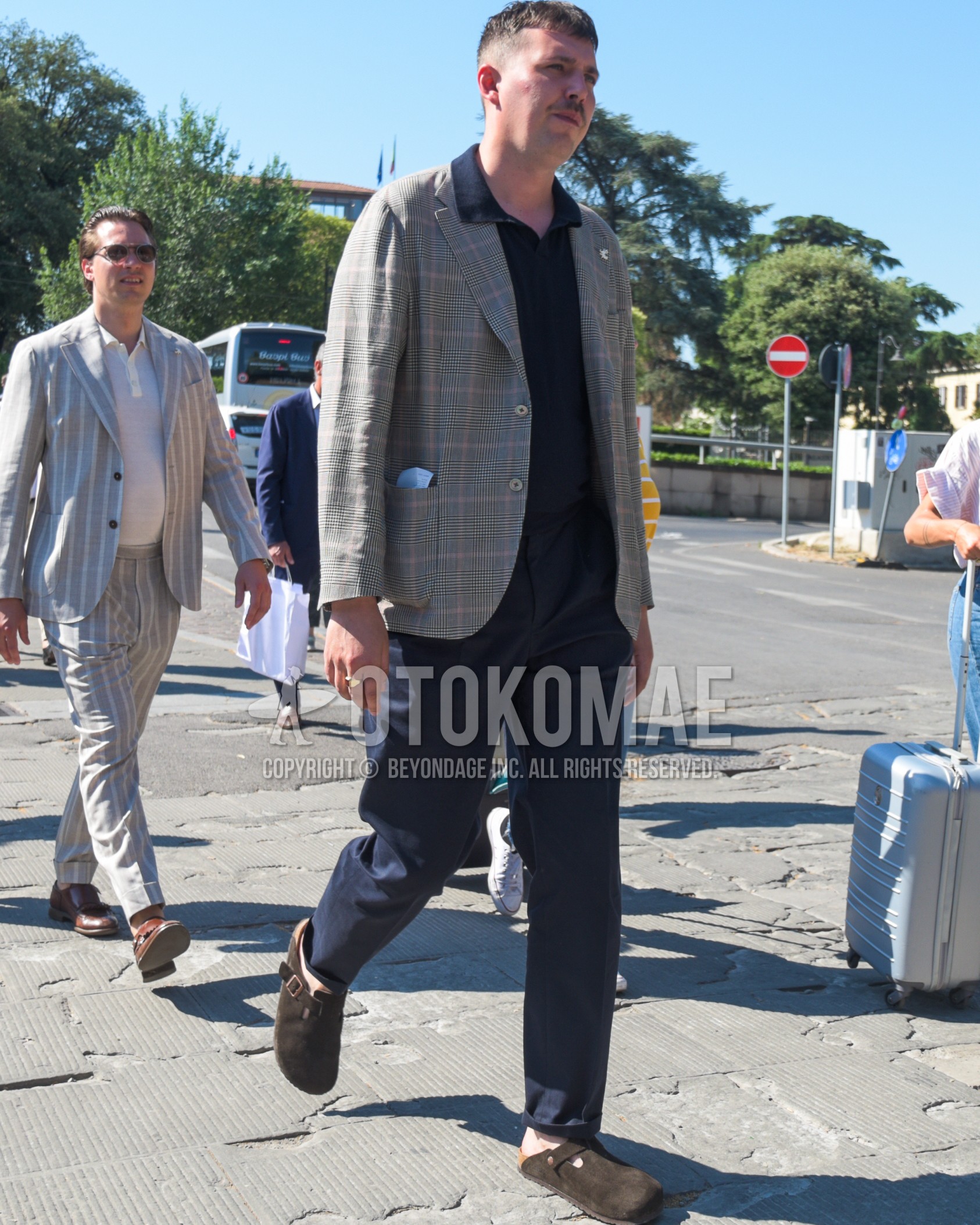 Men's spring summer outfit with gray check tailored jacket, black plain t-shirt, navy plain slacks, brown leather sandals.