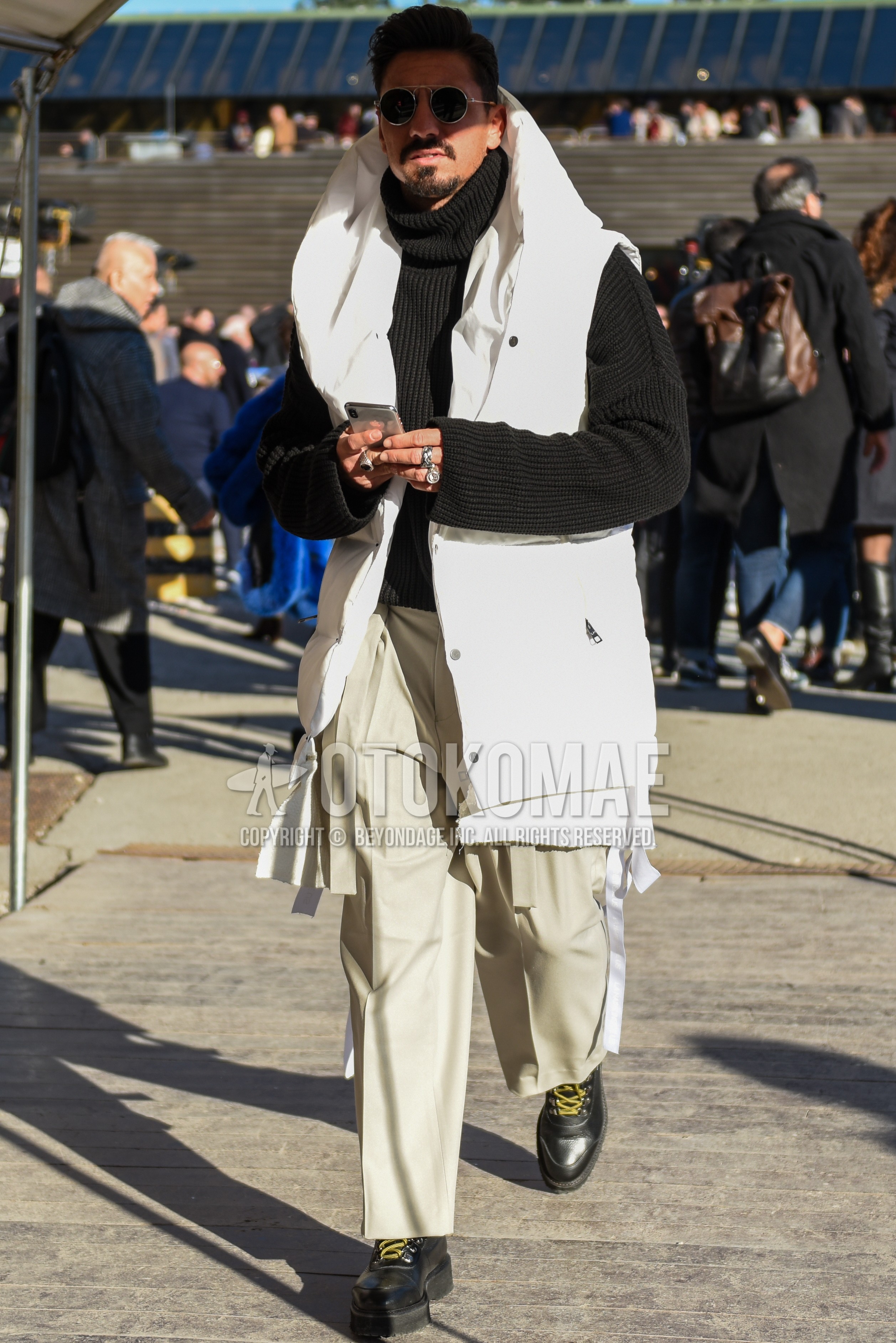 Men's autumn winter outfit with silver plain sunglasses, white plain casual vest, black plain turtleneck knit, beige plain chinos, beige plain ankle pants, black  boots.