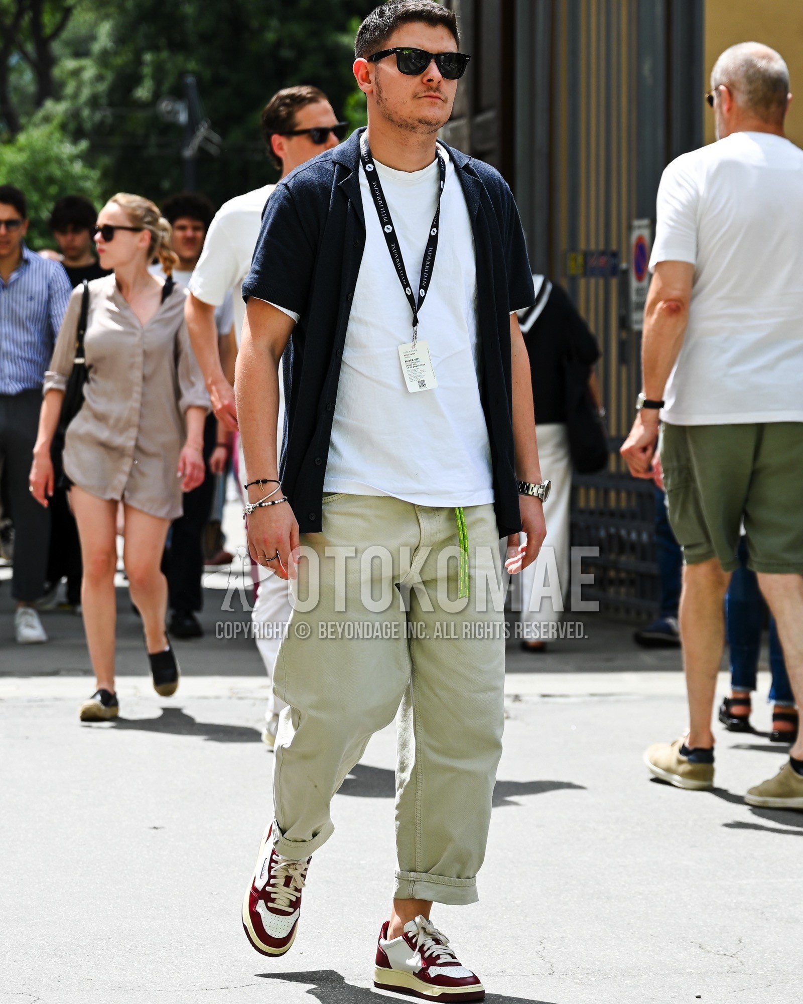 Men's spring summer outfit with black plain sunglasses, navy plain shirt, white plain t-shirt, beige plain chinos, white red low-cut sneakers.