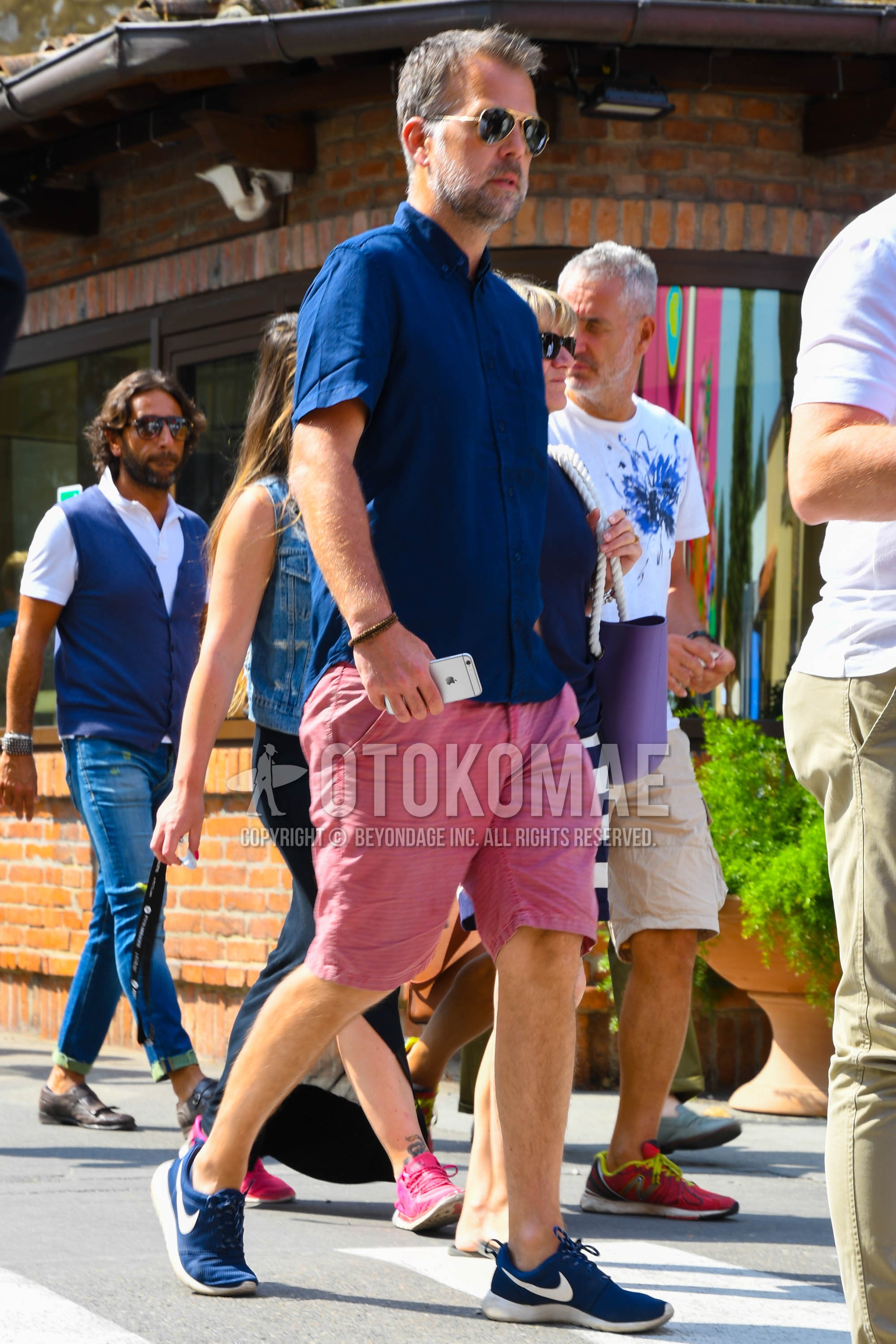 Men's summer outfit with plain sunglasses, blue plain shirt, red plain short pants, navy low-cut sneakers.