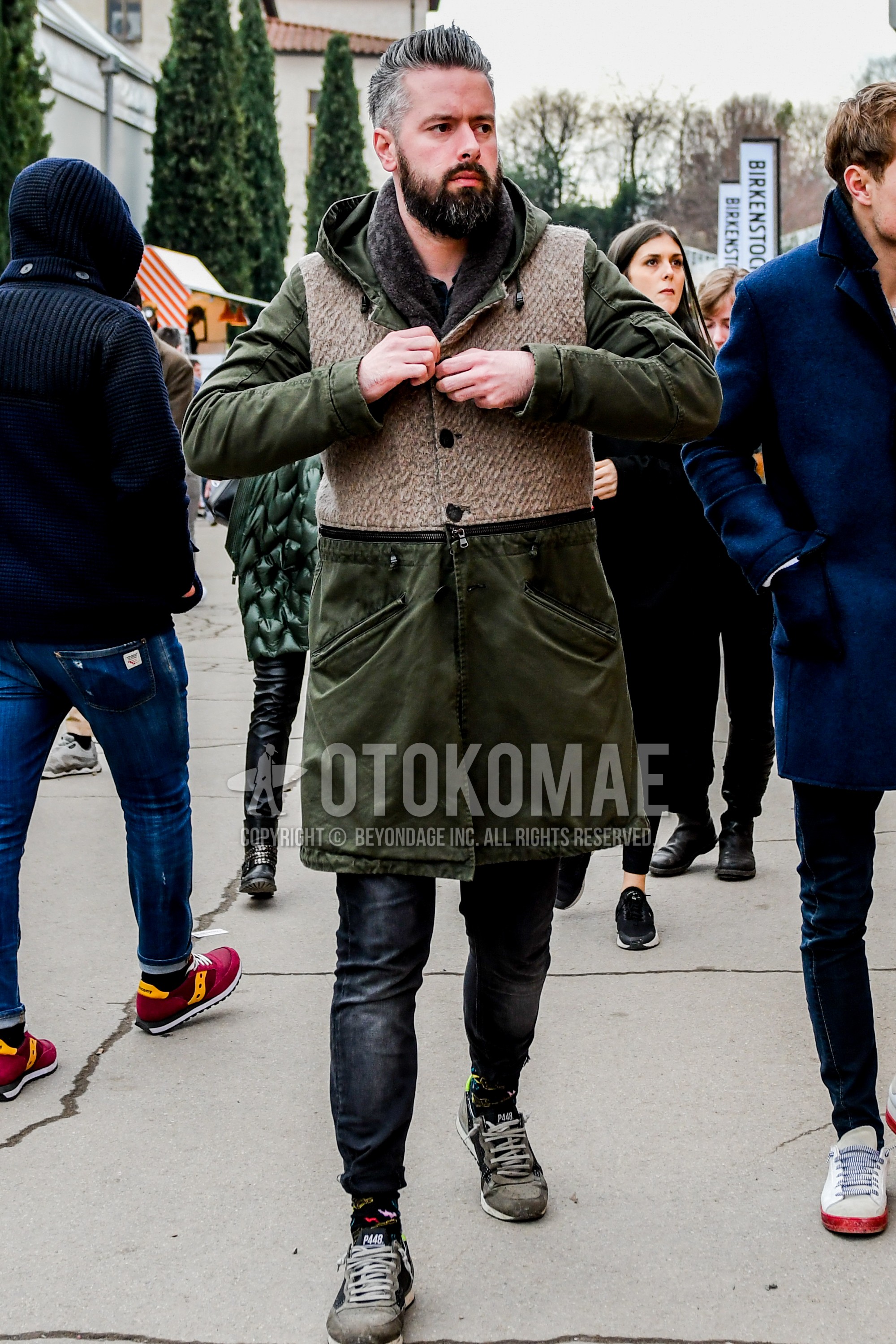Men's winter outfit with brown plain scarf, olive green plain hooded coat, dark gray plain denim/jeans, gray low-cut sneakers.