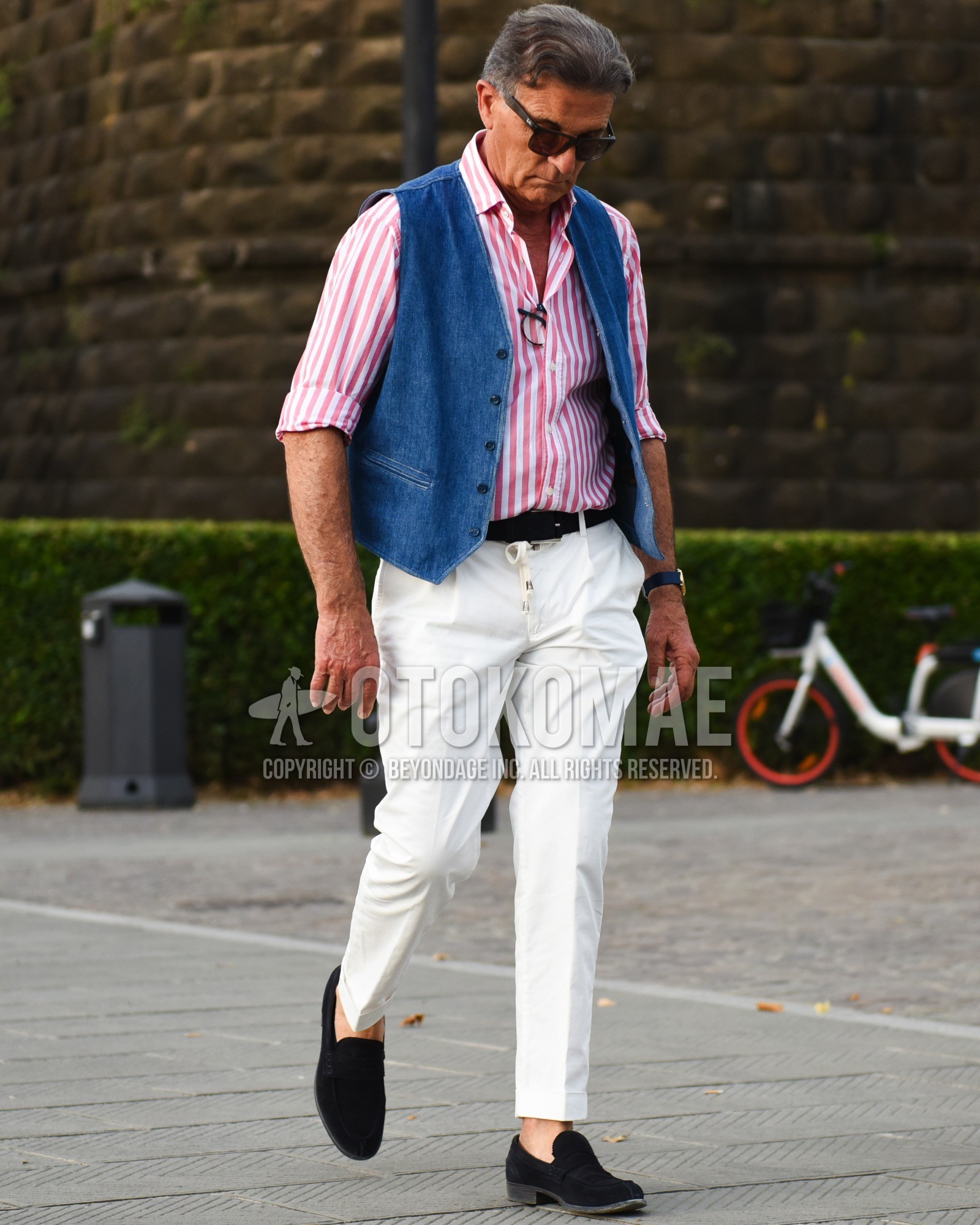 Men's spring summer outfit with black plain sunglasses, red stripes shirt, blue plain gilet, black plain leather belt, white plain slacks, white plain easy pants, black coin loafers leather shoes.