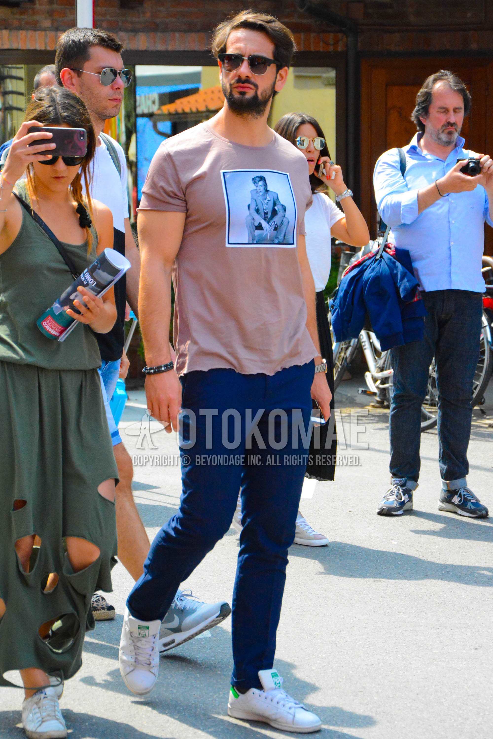 Men's spring summer outfit with black plain sunglasses, pink graphic t-shirt, navy plain chinos, white low-cut sneakers.