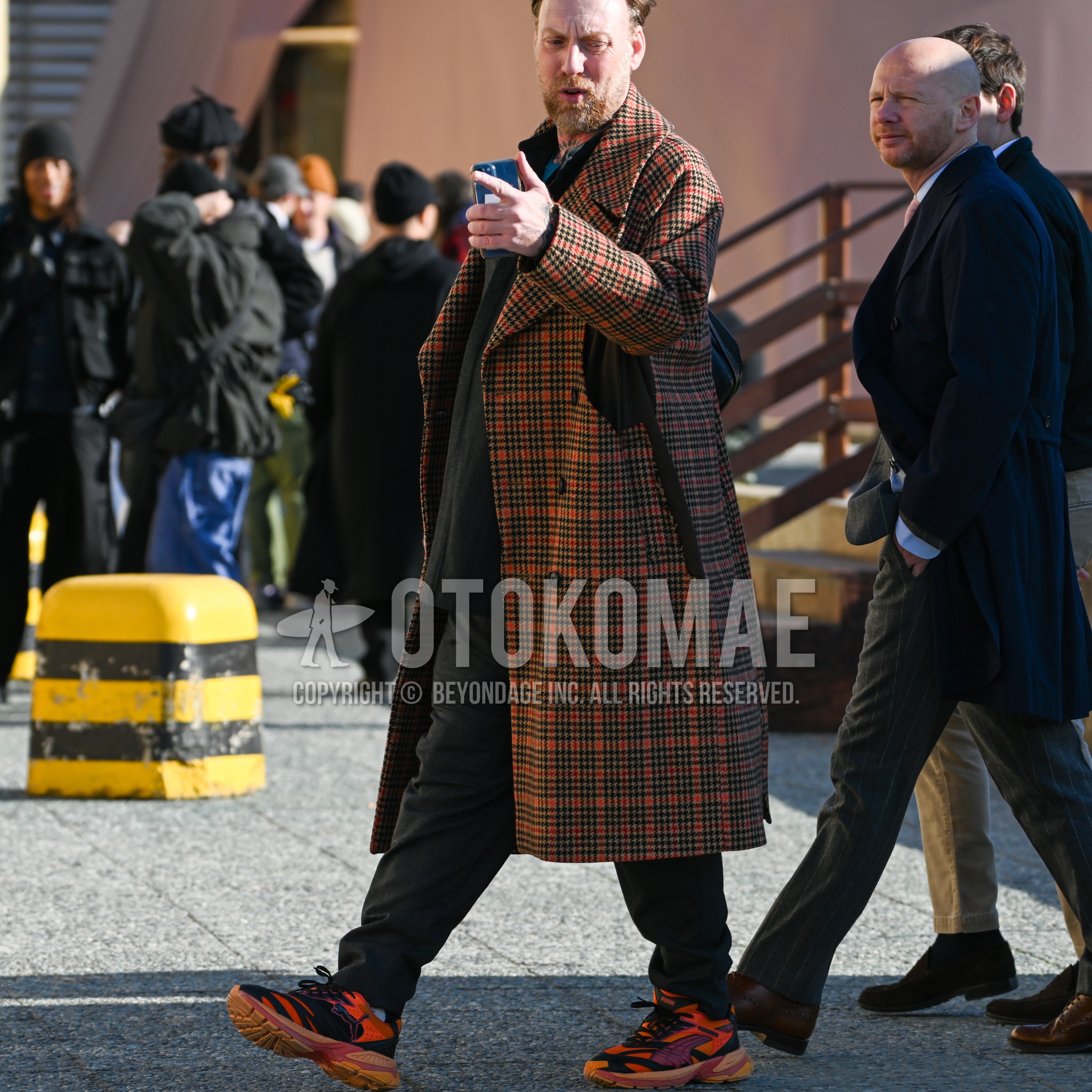 Men's autumn winter outfit with brown orange check chester coat, dark gray plain shirt, dark gray plain slacks, orange black multi-color low-cut sneakers.