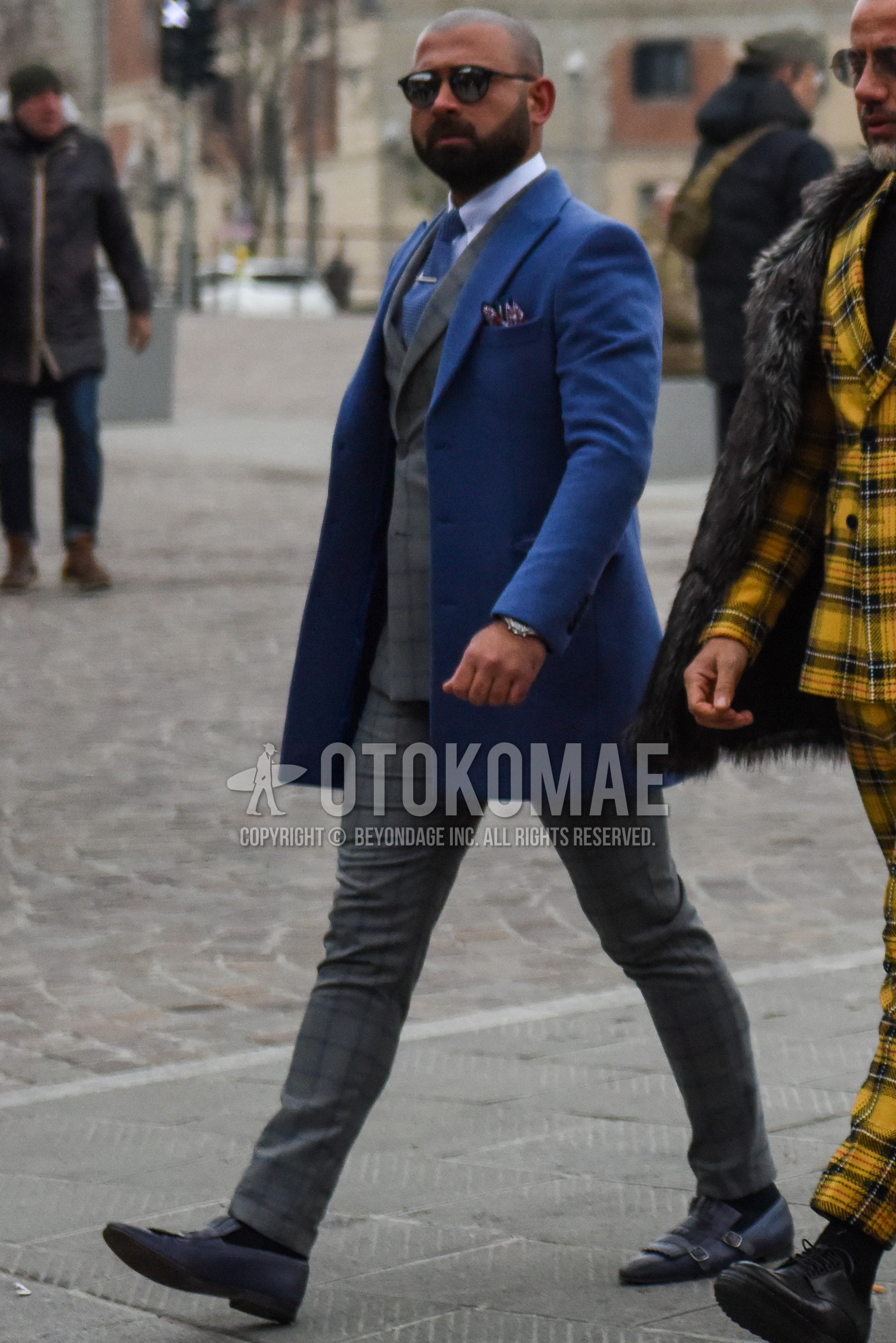 Men's winter outfit with plain sunglasses, blue plain chester coat, light blue plain shirt, navy monk shoes leather shoes, gray check suit, blue plain necktie.