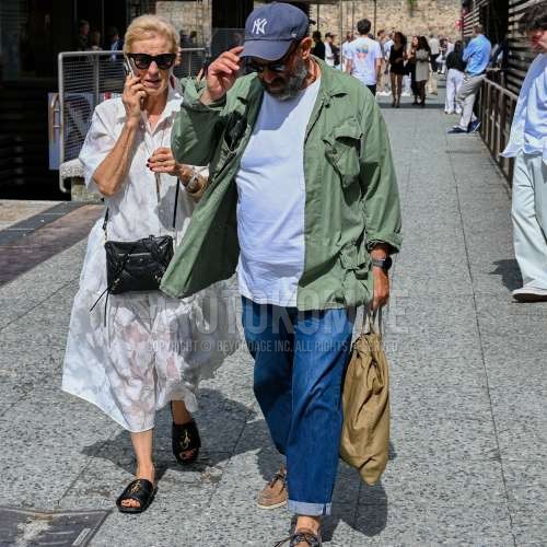 ネイビーレタードのベースボールキャップ、ブラウンべっ甲のサングラス、オリーブグリーン・グリーン無地のミリタリージャケット(MA-1、M-65以外)、白無地のTシャツ、ブルー無地のデニム/ジーンズ、ブラウンローファーの革靴、ベージュ無地のブリーフケース/ハンドバッグを合わせた春夏のメンズコーデ・着こなし。