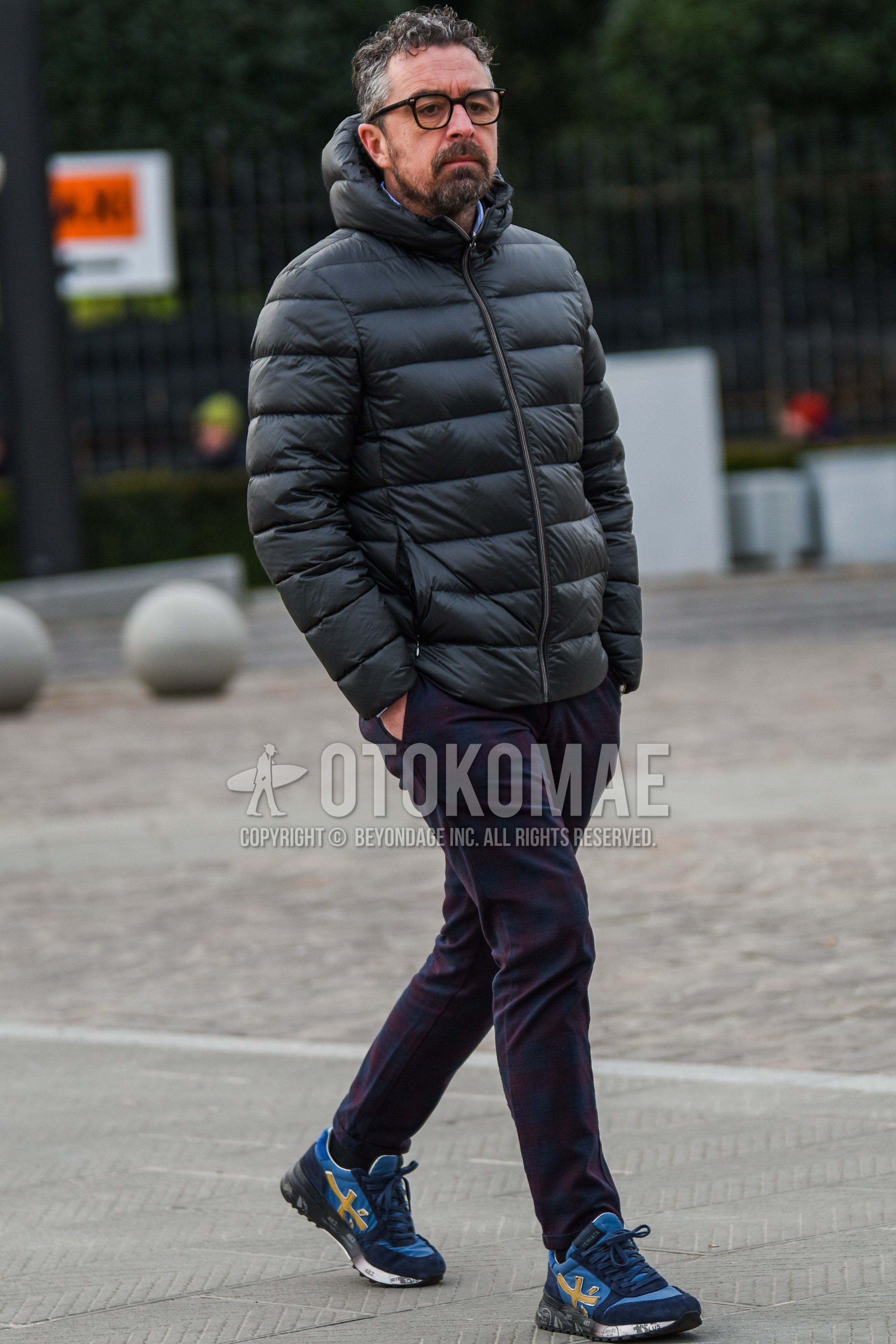 Men's autumn winter outfit with black plain glasses, black plain down jacket, navy red check slacks, blue low-cut sneakers.