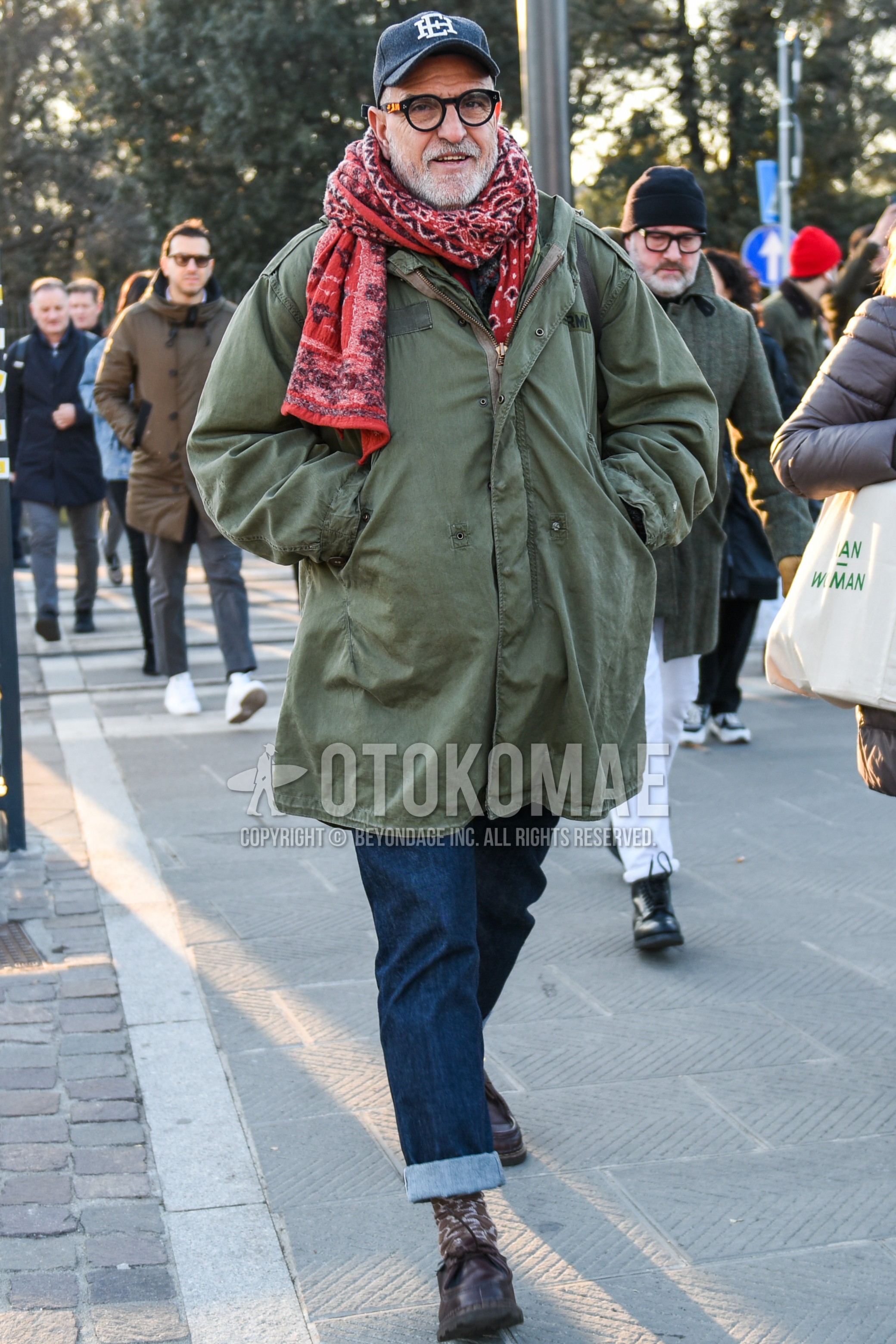 Men's autumn winter outfit with black one point baseball cap, black plain glasses, red scarf scarf, green plain field jacket/hunting jacket, blue plain denim/jeans, brown socks socks, brown  loafers leather shoes.