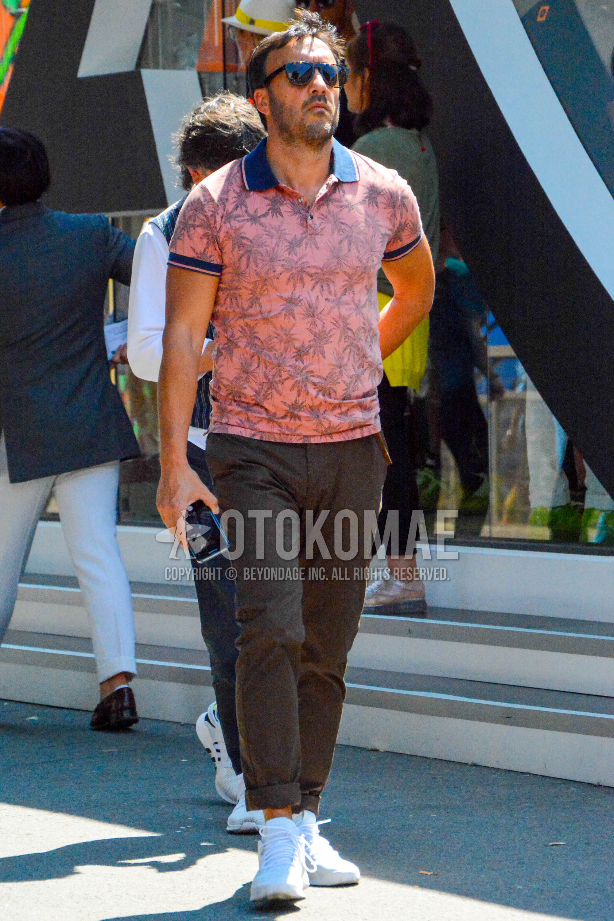 Men's spring summer outfit with brown tortoiseshell sunglasses, pink botanical polo shirt, brown plain chinos, white high-cut sneakers.