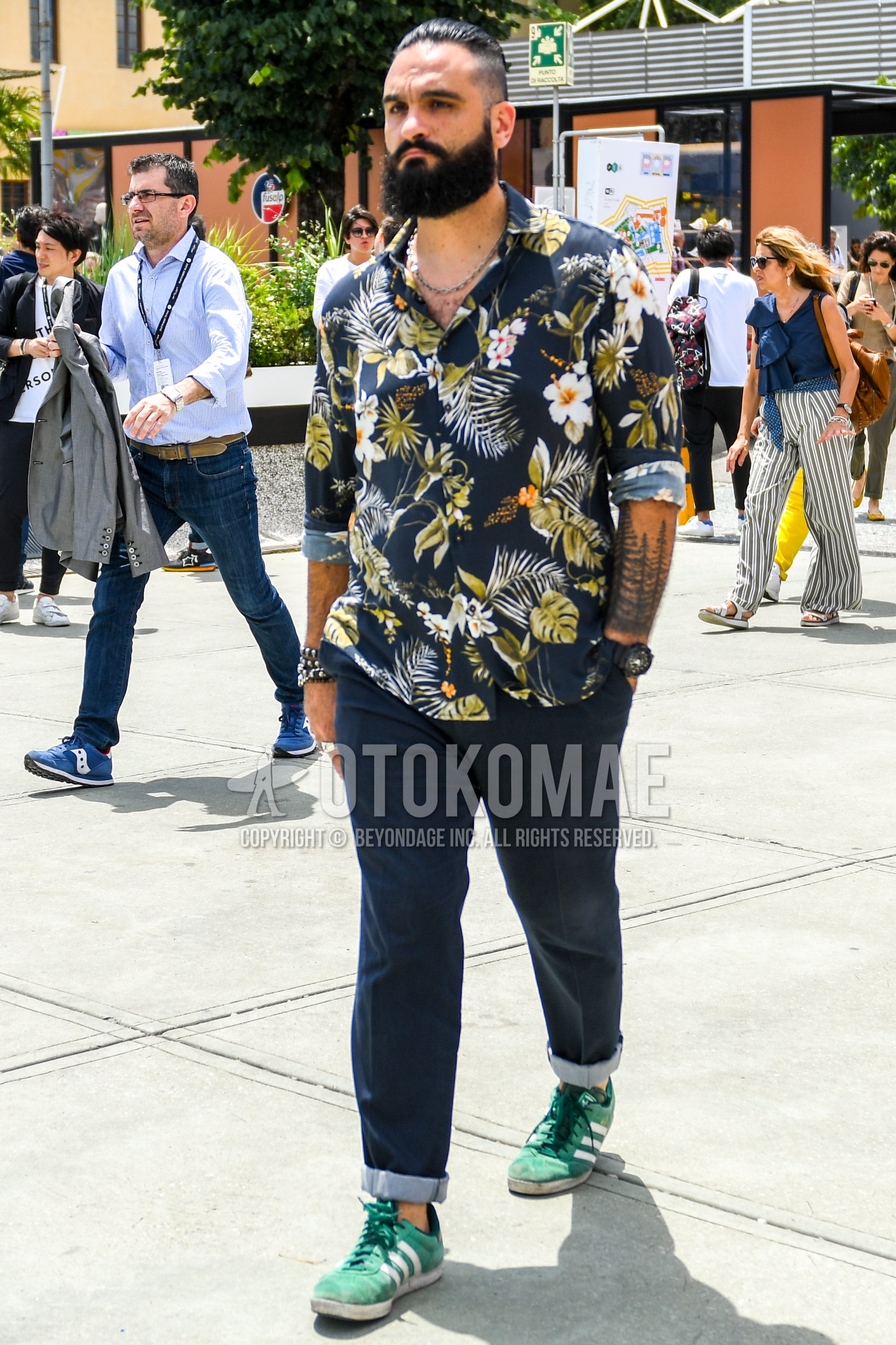 Men's summer outfit with navy botanical shirt, black plain denim/jeans, green low-cut sneakers.