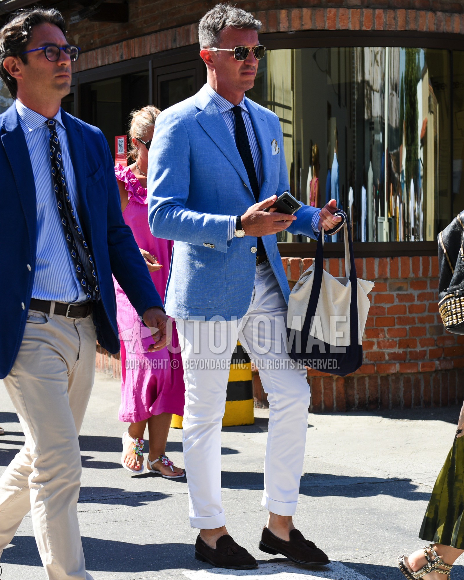 Men's spring summer outfit with gold plain sunglasses, blue plain tailored jacket, blue stripes shirt, brown plain leather belt, white plain slacks, white plain tote bag, navy plain necktie.
