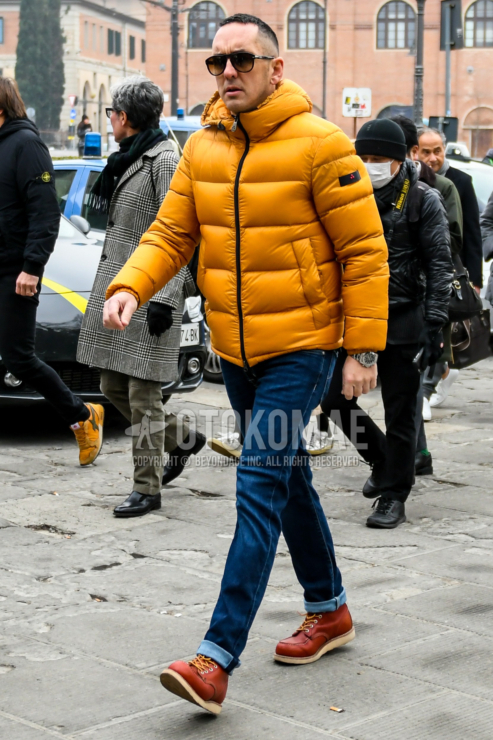 Men's winter outfit with plain sunglasses, yellow plain down jacket, blue plain denim/jeans, brown work boots.