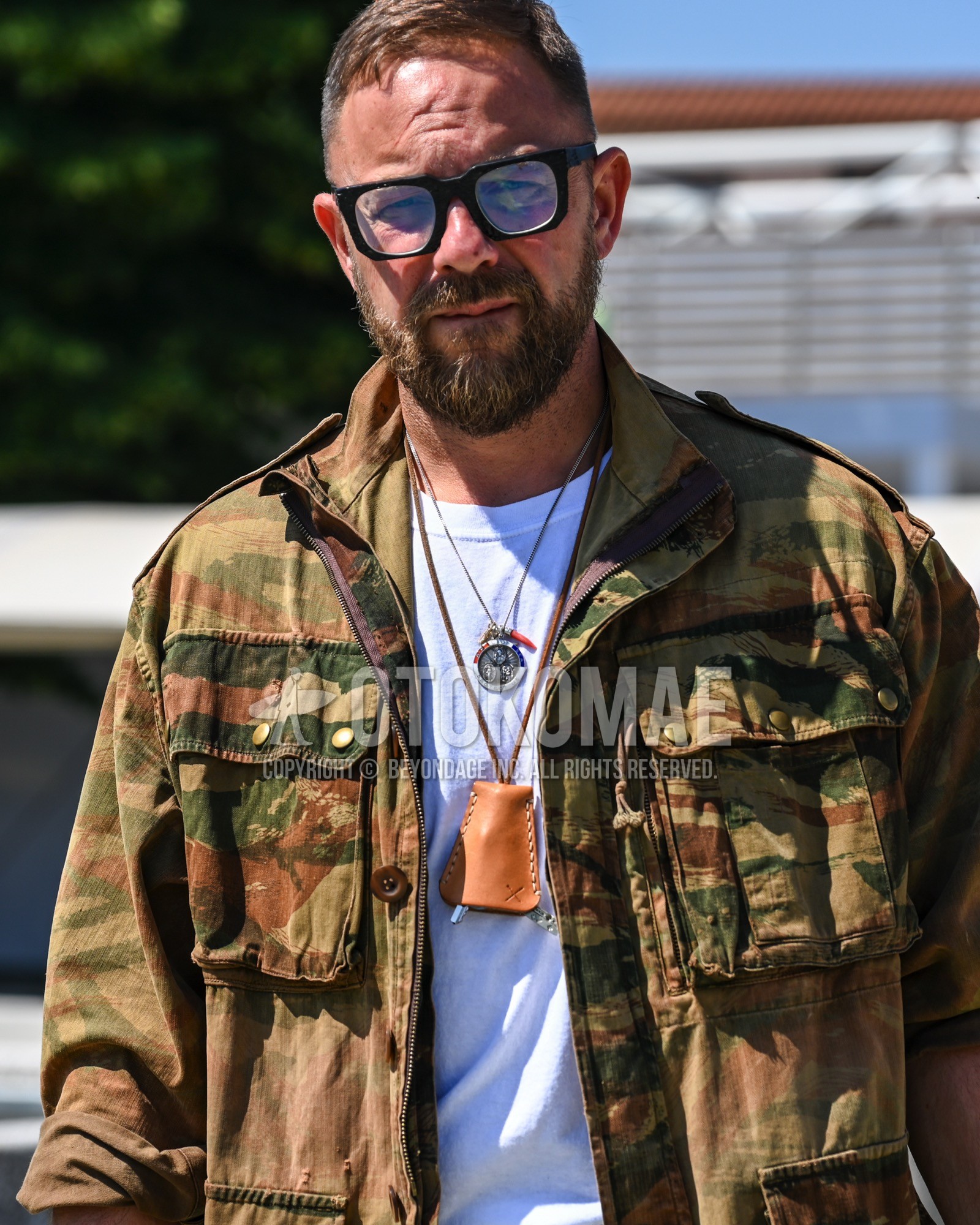 Men's spring summer autumn outfit with clear plain sunglasses, olive green camouflage military jacket, white plain t-shirt.