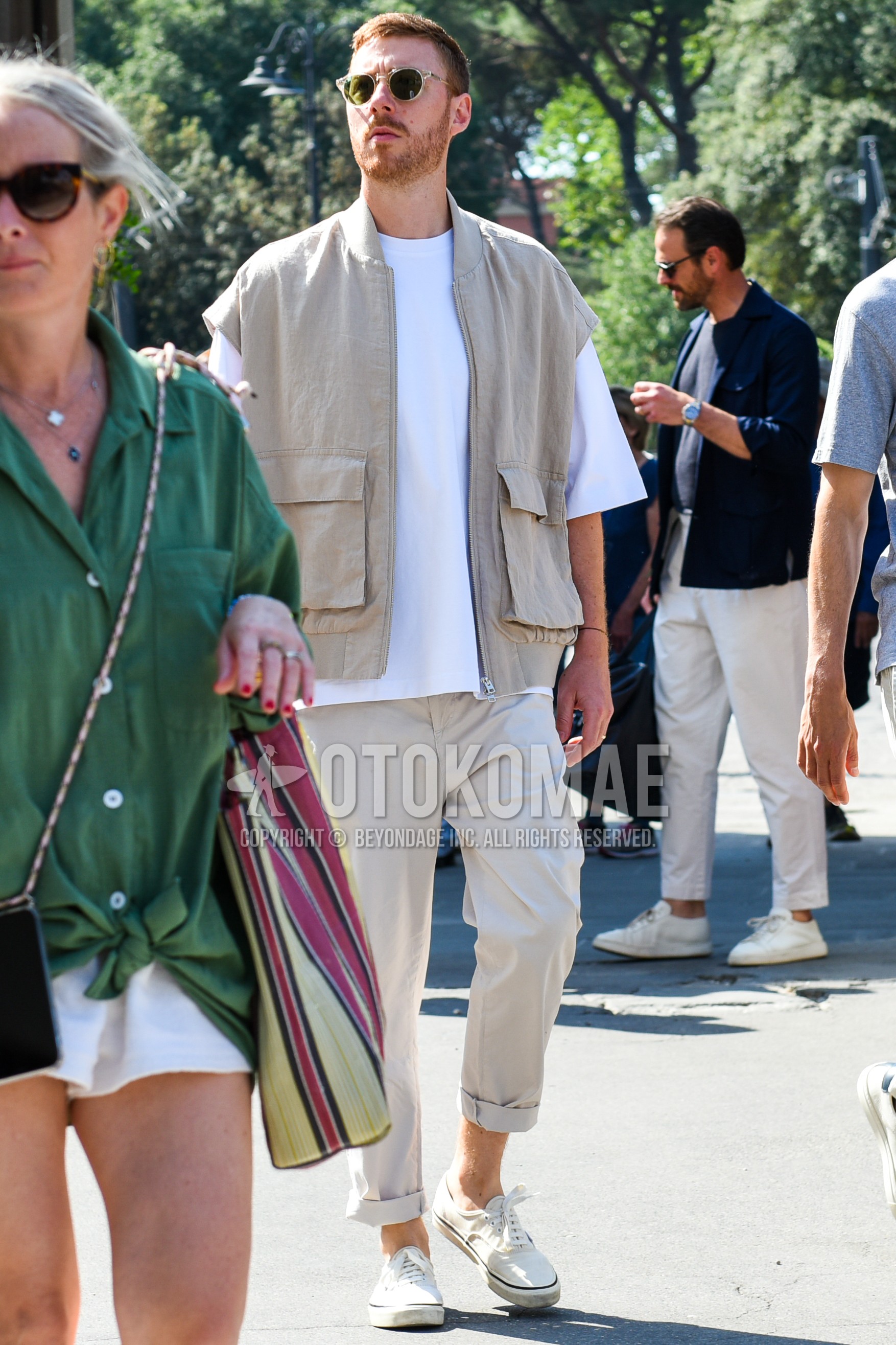 Men's spring summer outfit with clear plain sunglasses, beige plain casual vest, white plain t-shirt, beige plain chinos, white low-cut sneakers.