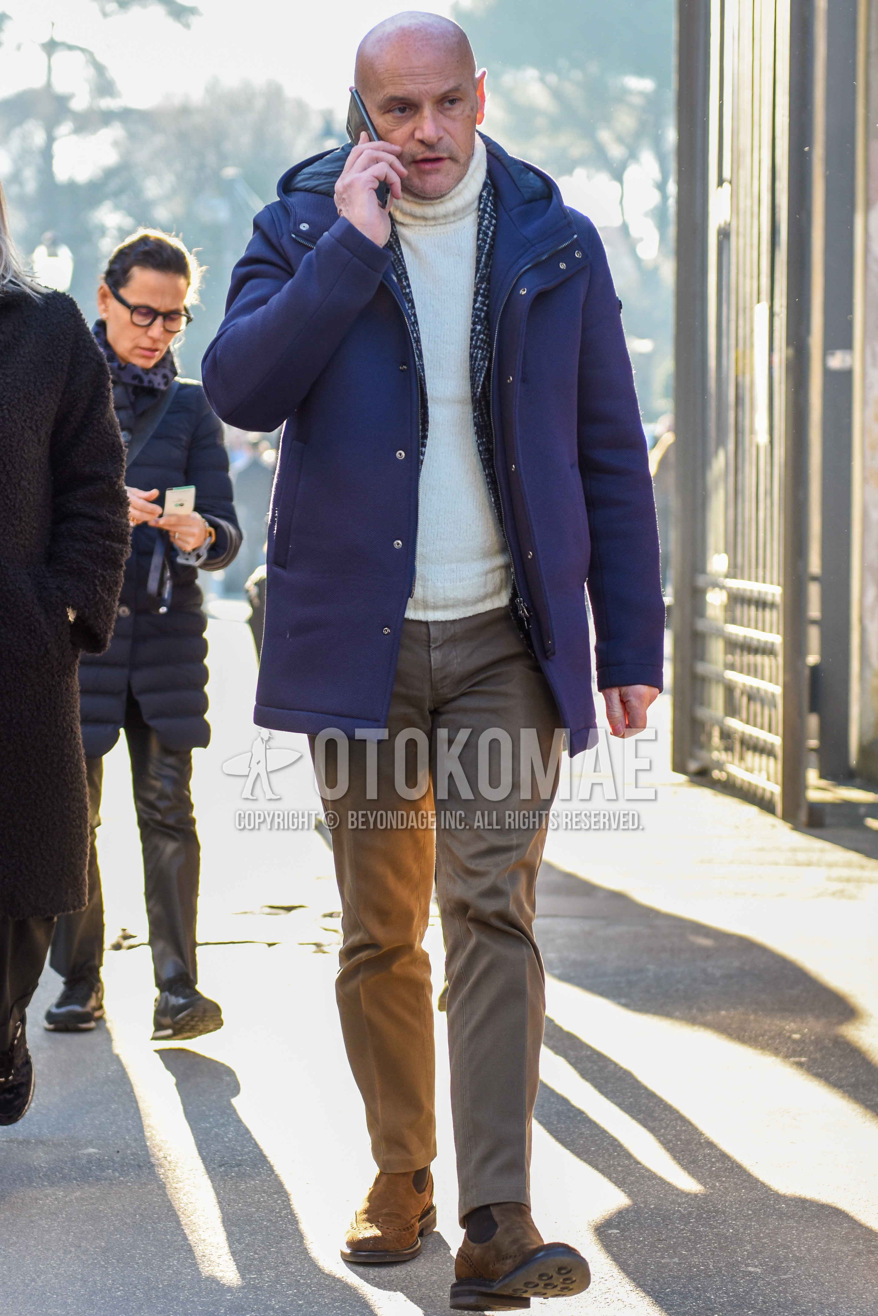 Men's autumn winter outfit with gray plain hooded coat, navy check tailored jacket, white plain turtleneck knit, beige plain chinos, beige side-gore boots.