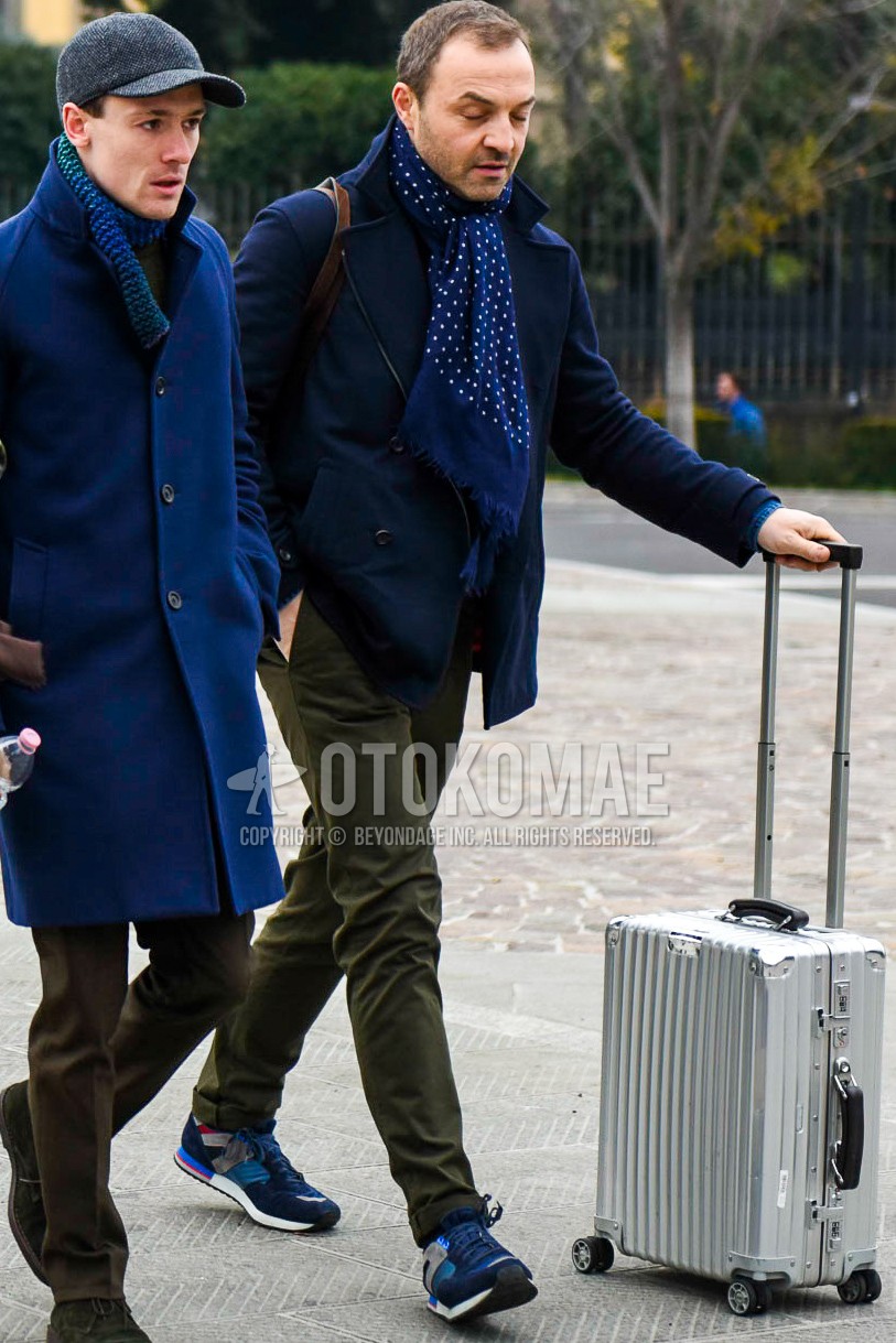 Men's autumn winter outfit with navy dots scarf, navy plain p coat, olive green plain chinos, navy low-cut sneakers, silver plain suitcase.