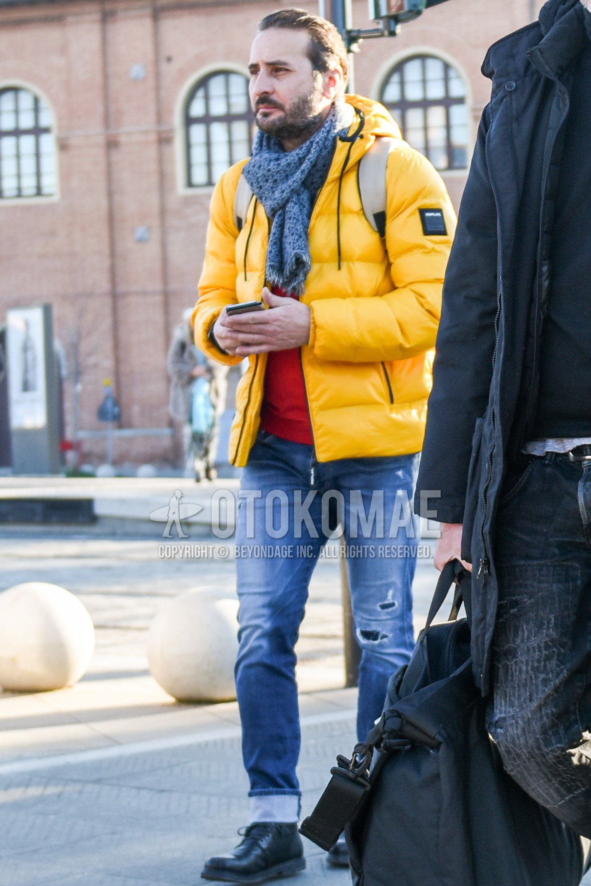 Men's winter outfit with gray scarf scarf, yellow plain down jacket, orange plain sweater, blue plain damaged jeans, black  boots.