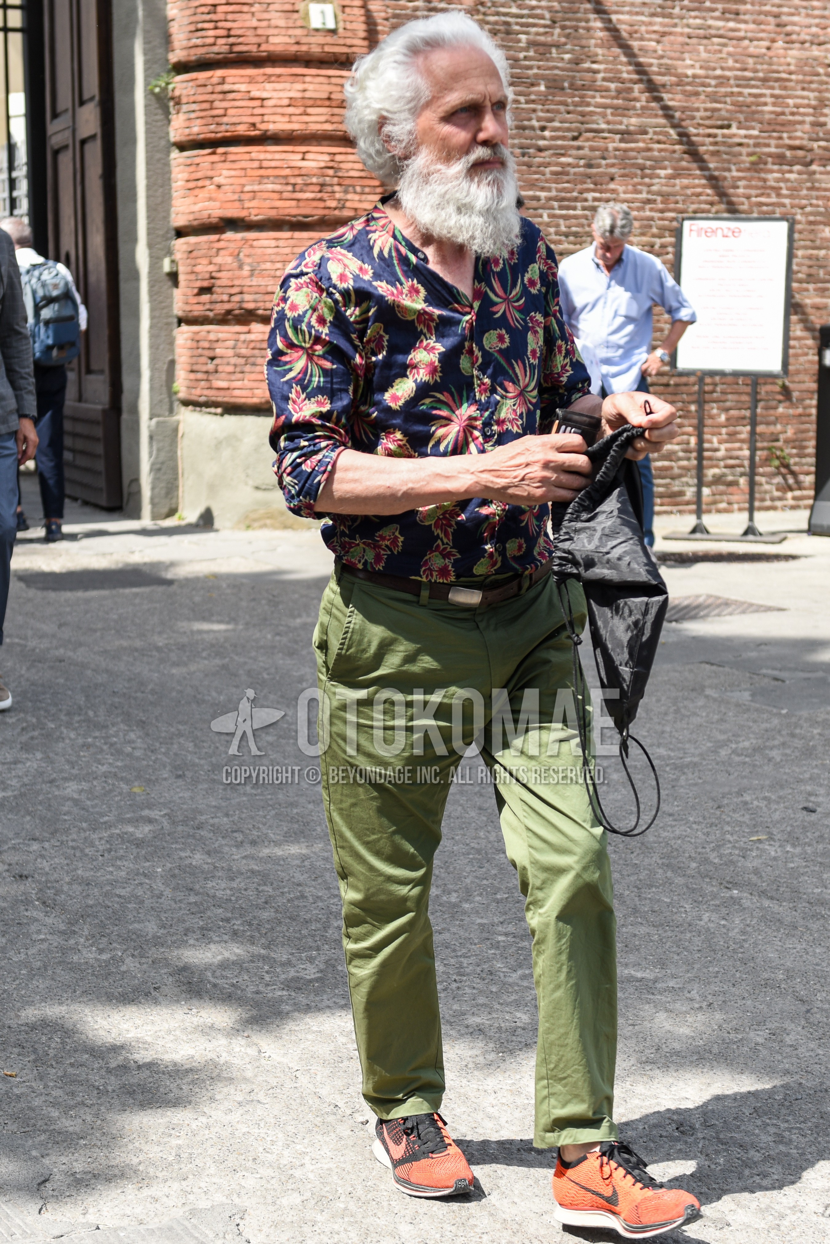 Men's summer outfit with navy multi-color botanical shirt, brown plain leather belt, olive green plain cotton pants, orange low-cut sneakers.