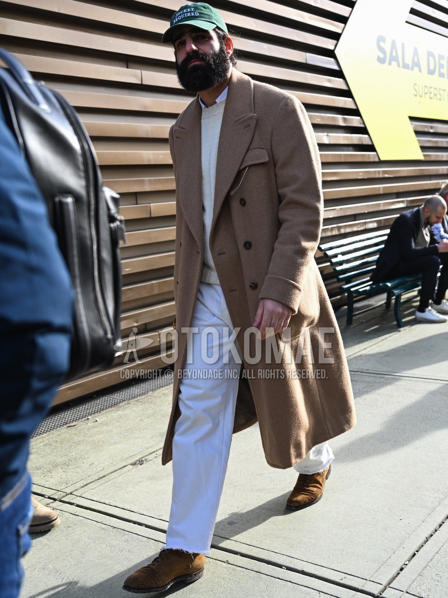 Men's autumn winter outfit with green deca logo baseball cap, beige plain chester coat, white plain shirt, white plain sweater, white plain denim/jeans, brown plain toe leather shoes.