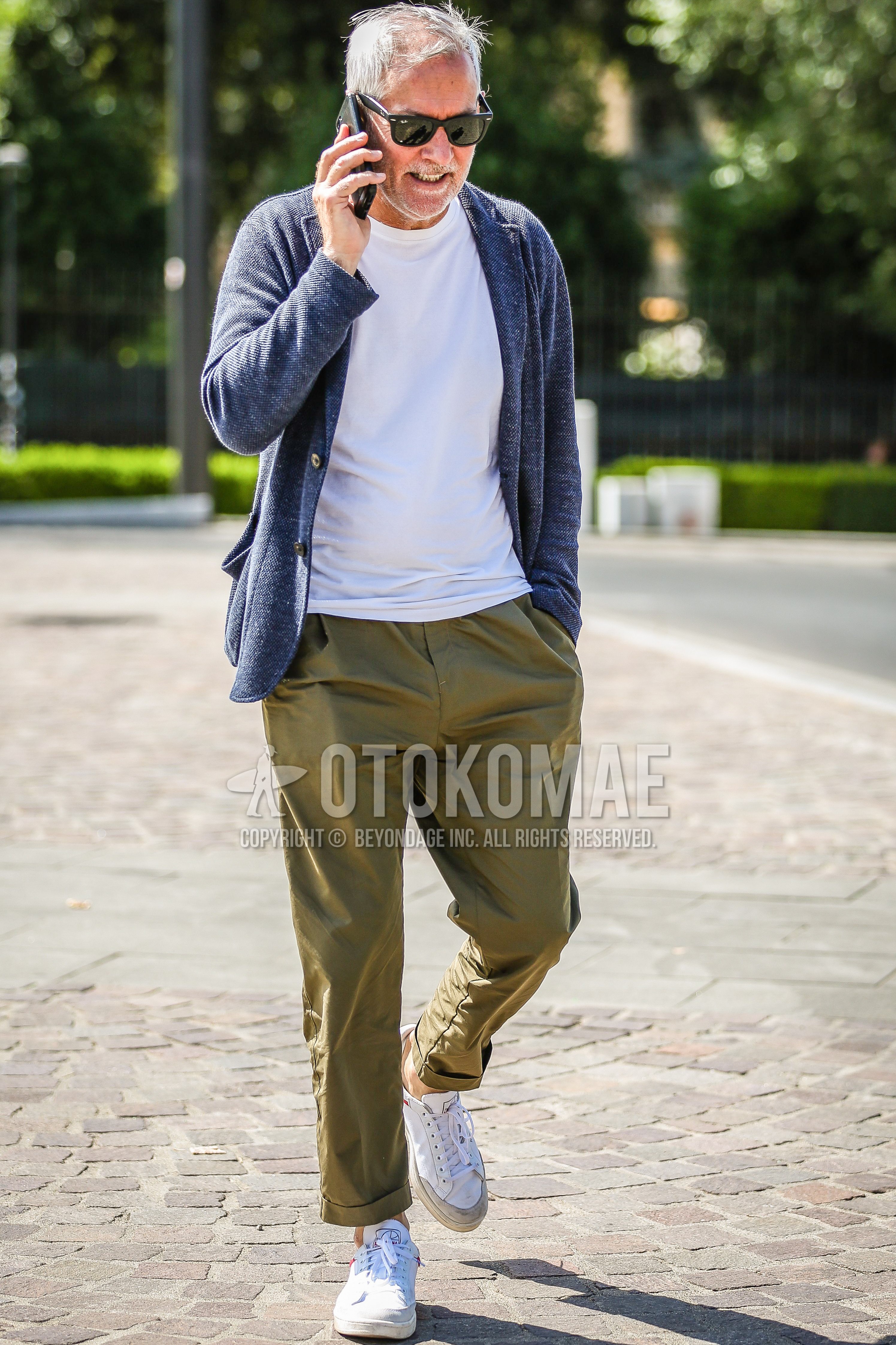 Men's spring summer outfit with black plain sunglasses, blue outerwear tailored jacket, white plain t-shirt, olive green plain chinos, white sneakers.