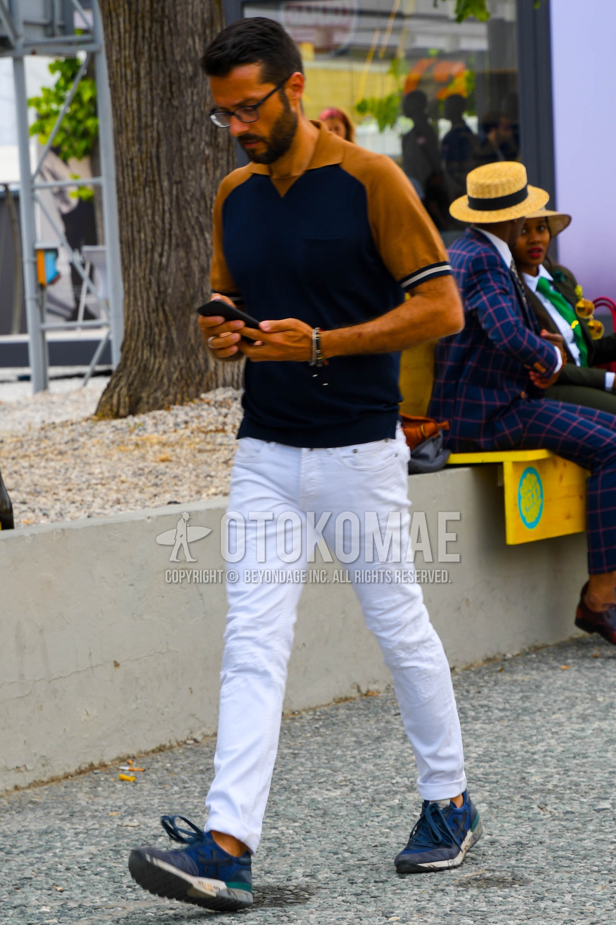 Men's summer outfit with plain glasses, beige navy plain polo shirt, white plain denim/jeans, navy low-cut sneakers.