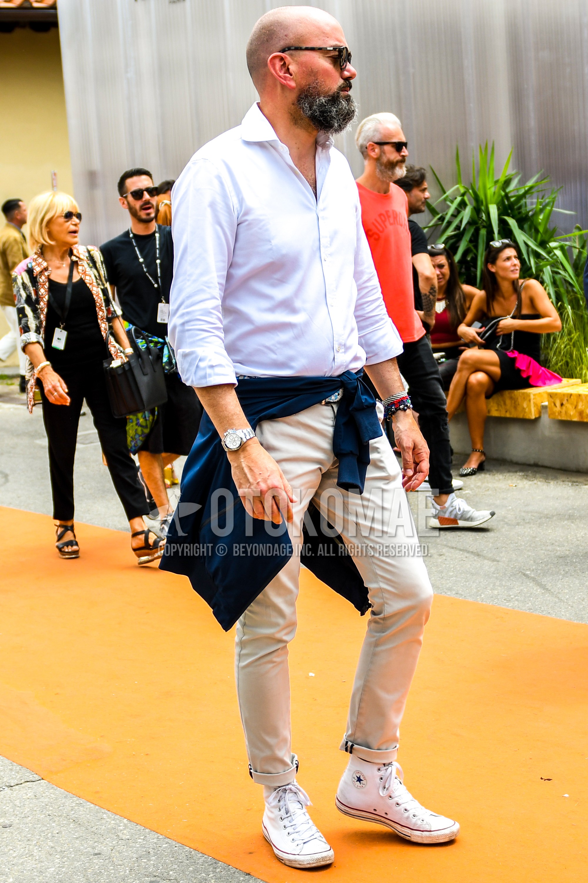Men's spring summer outfit with plain sunglasses, white plain shirt, beige plain chinos, white high-cut sneakers.