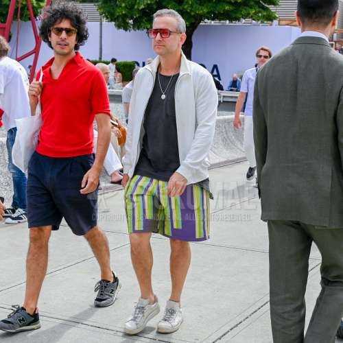 黒無地のサングラス、白無地のアウター、黒無地のTシャツ、マルチカラーボトムスのショートパンツ、白ローカットのスニーカーを合わせた夏春のメンズコーデ・着こなし。