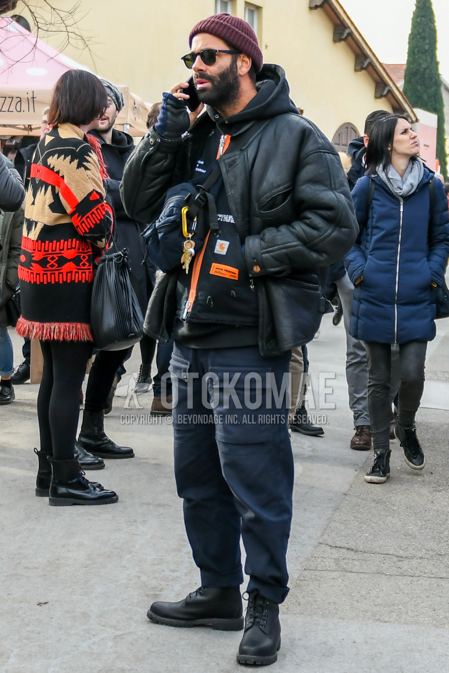Men's winter outfit with red plain knit cap, plain sunglasses, black plain leather jacket, black plain hoodie, gray plain cargo pants, black  boots, black plain shoulder bag.