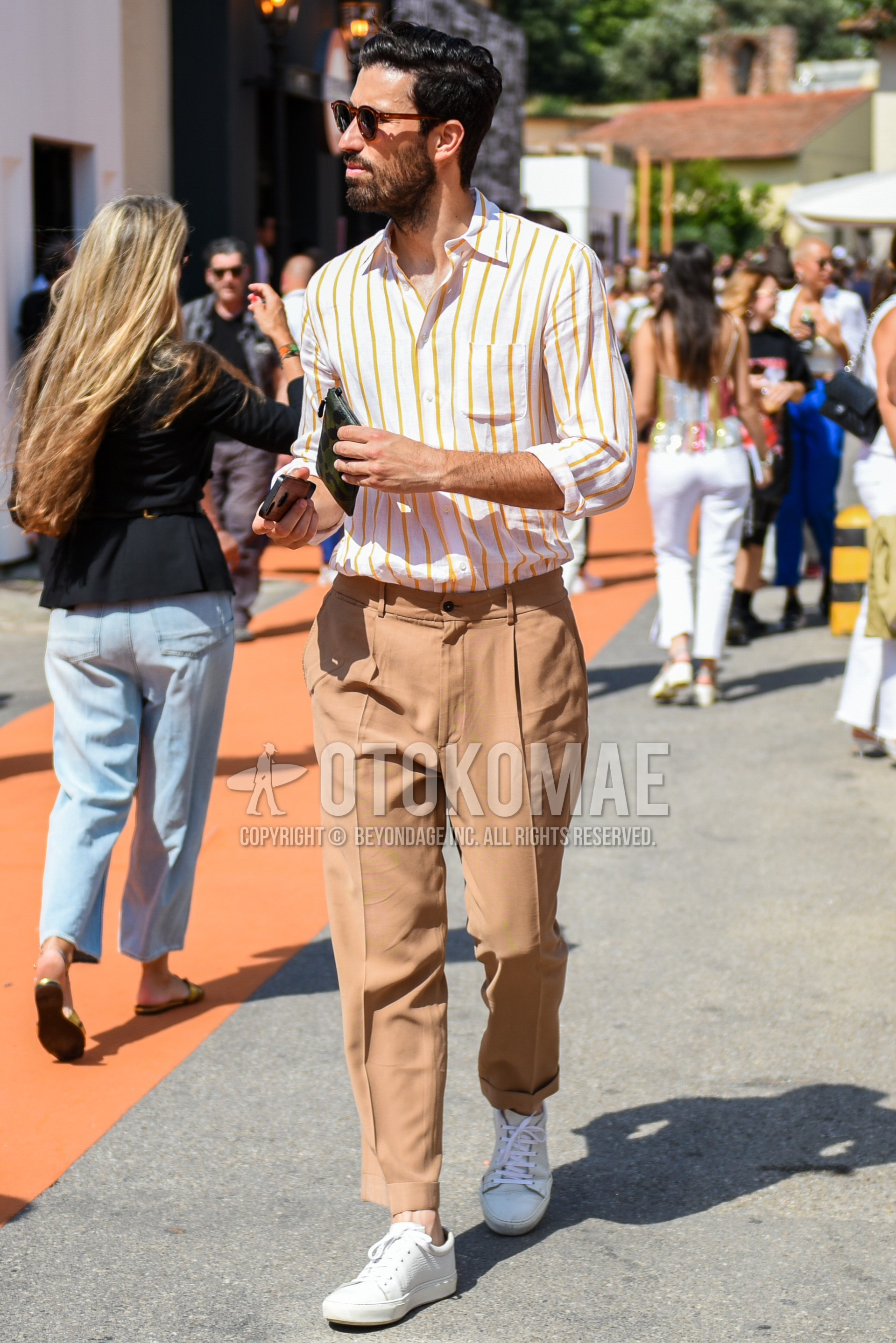 Men's spring summer autumn outfit with brown tortoiseshell sunglasses, yellow white stripes shirt, beige plain slacks, beige plain ankle pants, white low-cut sneakers.