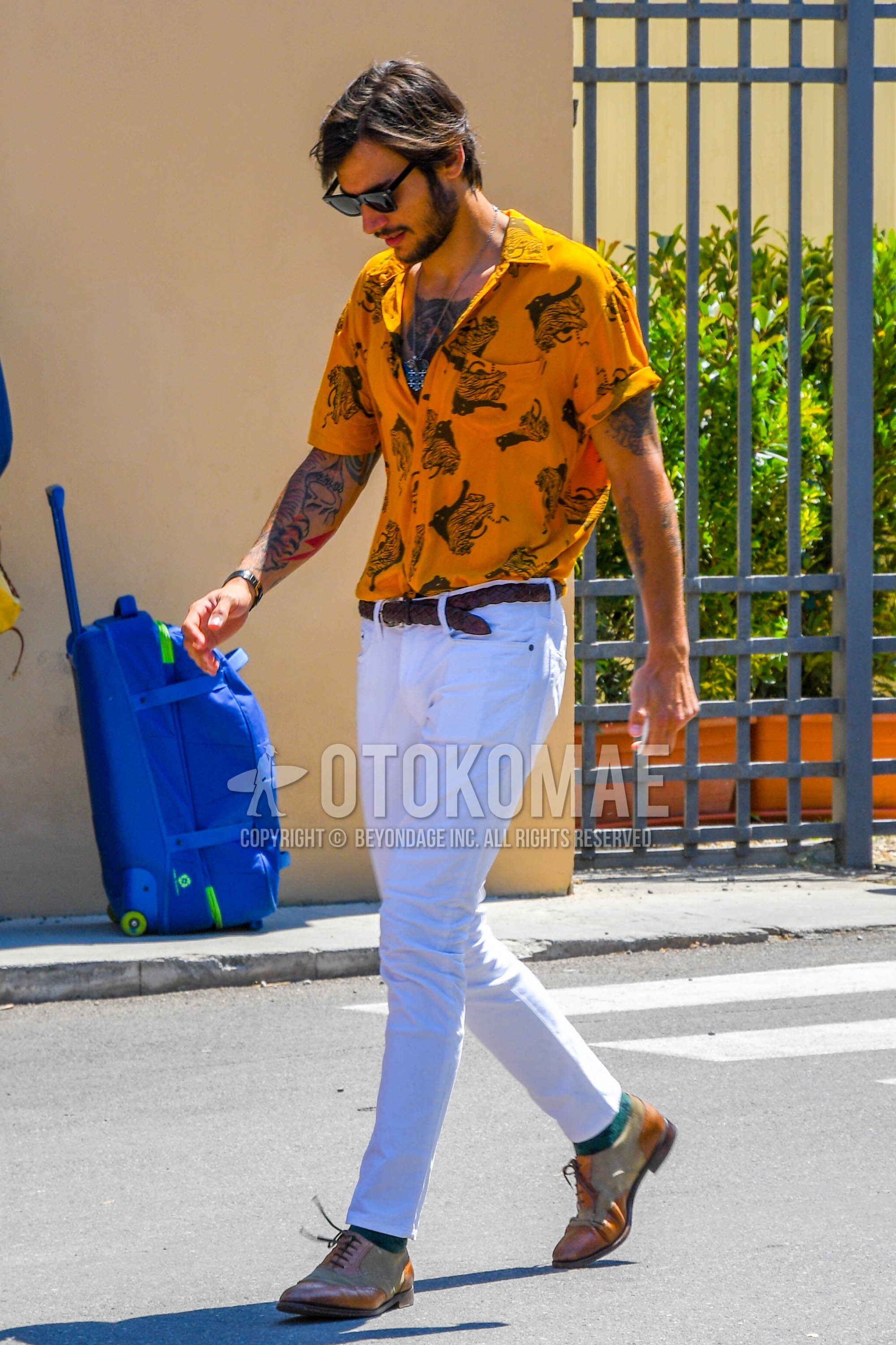 Men's spring summer outfit with black plain sunglasses, yellow graphic shirt, brown plain braided belt, white plain denim/jeans, green plain socks, brown straight-tip shoes leather shoes.