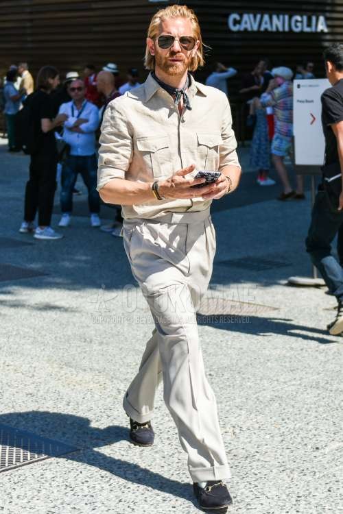 ティアドロップの黒・ゴールド無地のサングラス、黒ストールのバンダナ/ネッカチーフ、リネンのベージュ無地のシャツ、グレー無地のベルトレスパンツ、水色無地のソックス、スエードの黒ビットローファーの革靴を合わせた夏のメンズコーデ・着こなし。