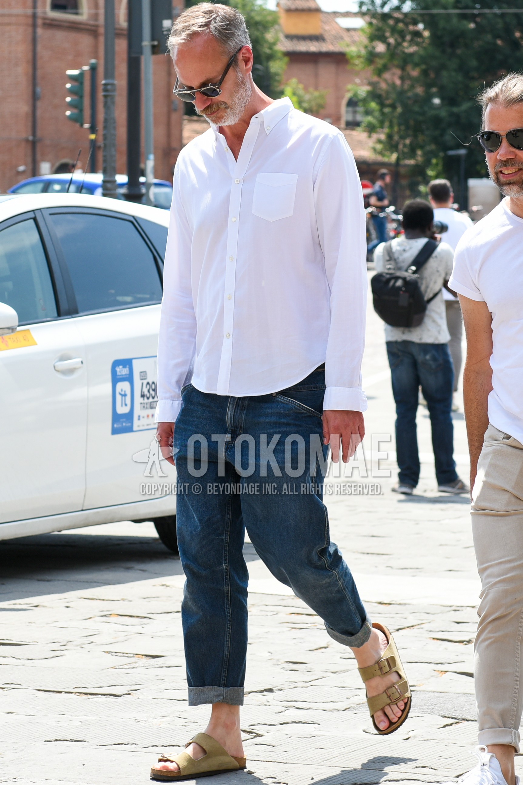 Men's spring summer outfit with black plain sunglasses, white plain shirt, blue plain denim/jeans, beige leather sandals.