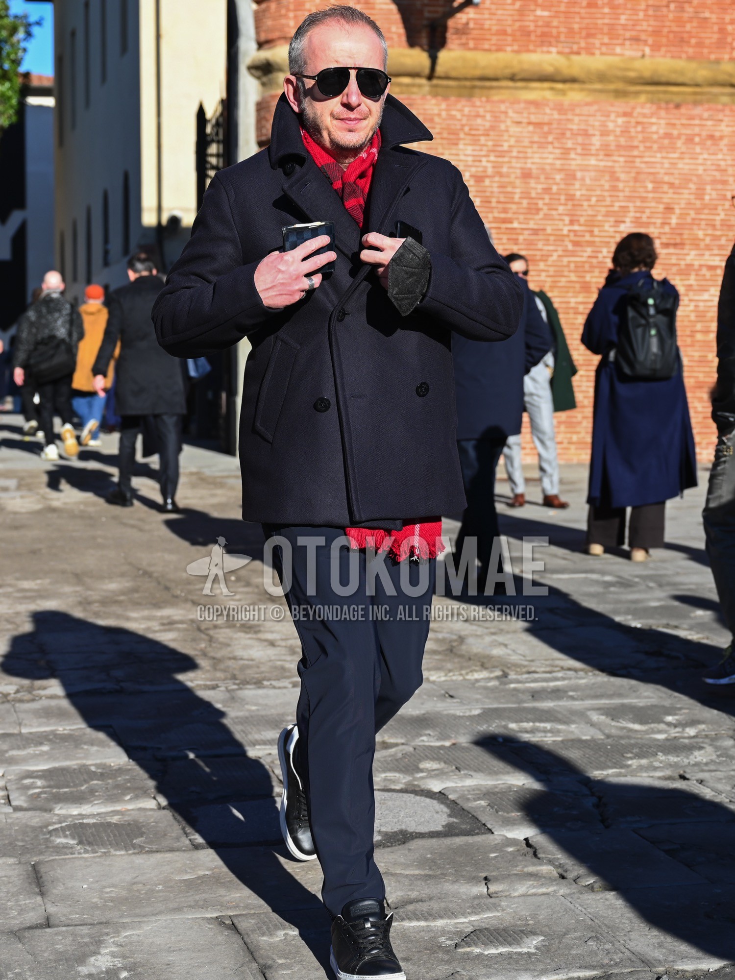 Men's autumn winter outfit with black plain sunglasses, red check scarf, navy plain ulster coat, navy plain slacks, black low-cut sneakers.